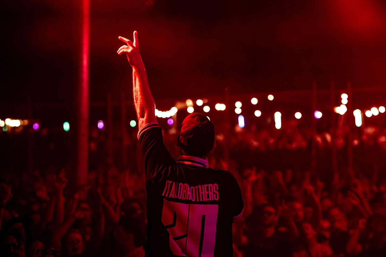 Performer in ITALOBORTHERS jersey making rock sign to large outdoor festival crowd at night.