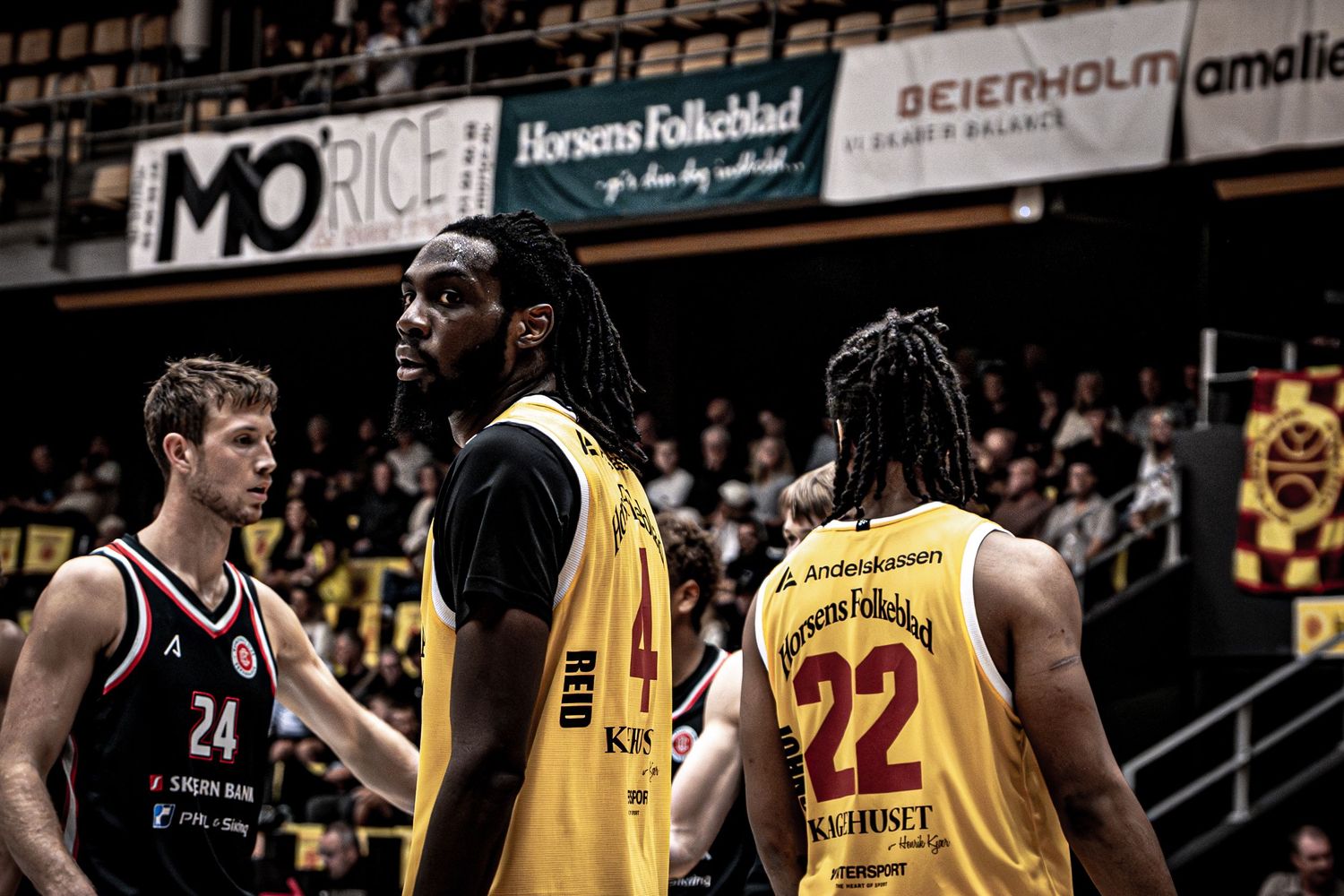 Three basketball players standing on court during game, two in yellow jerseys.