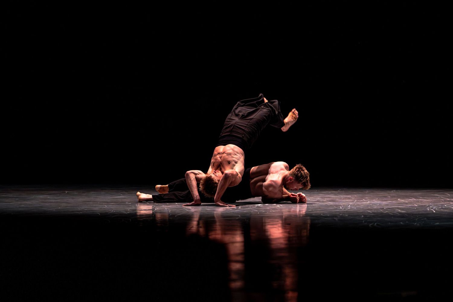 Two dancers performing an intense floor-based contemporary dance routine on a reflective stage.