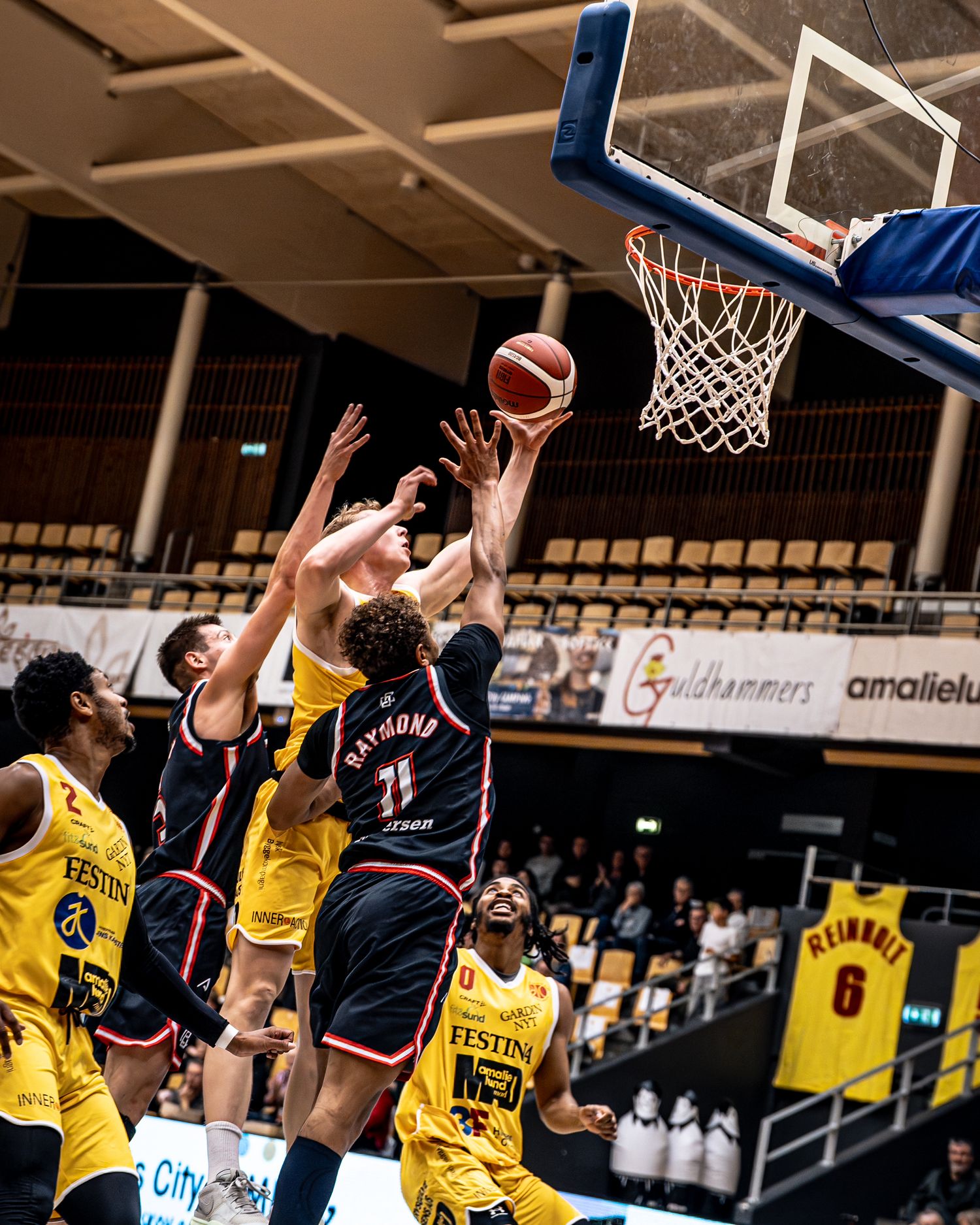 Player number 11 in dark jersey attempts layup against yellow team defenders in basketball game.