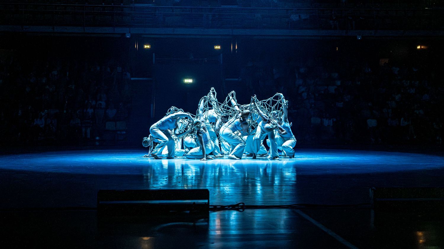 Dancers huddle together in dramatic blue stage lighting during a captivating live performance.