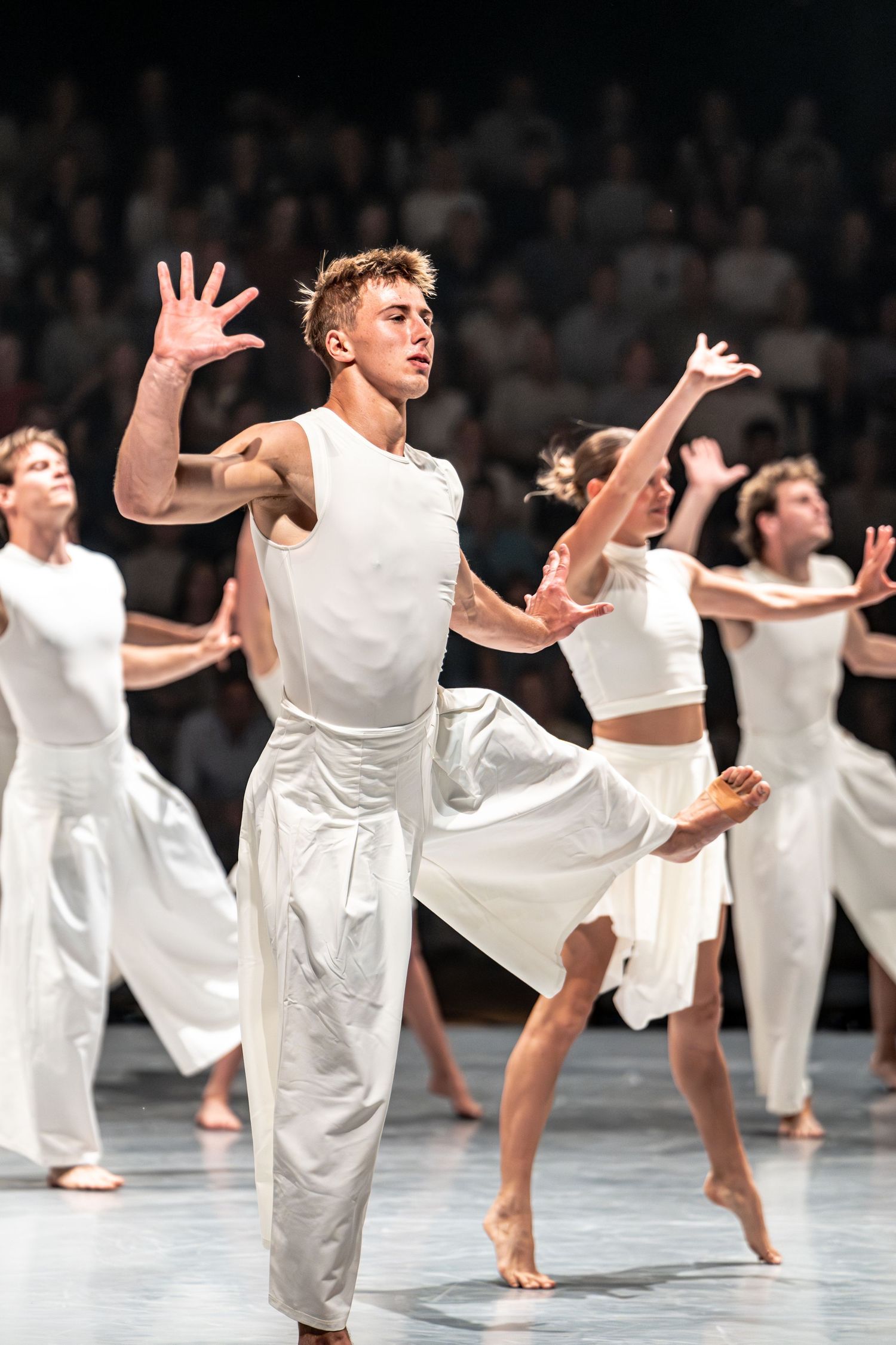 Contemporary dancers in white attire perform dynamic choreography on a professional stage.