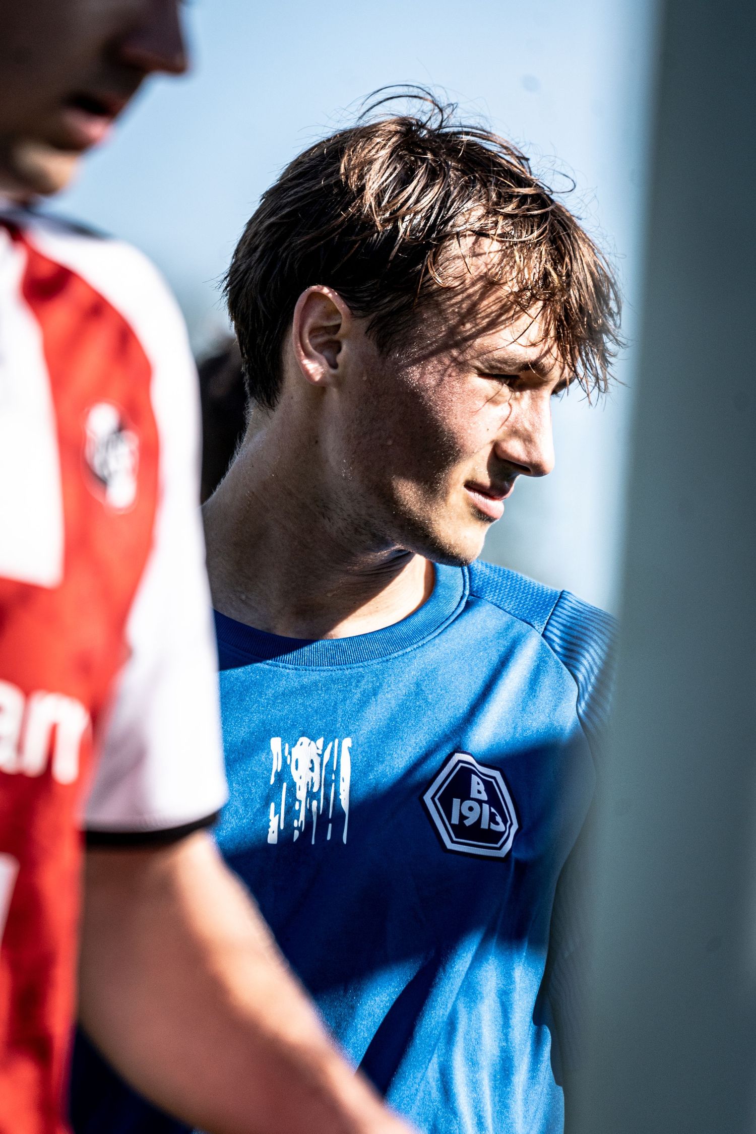 Close-up portrait of a focused male soccer player in blue jersey with club badge.