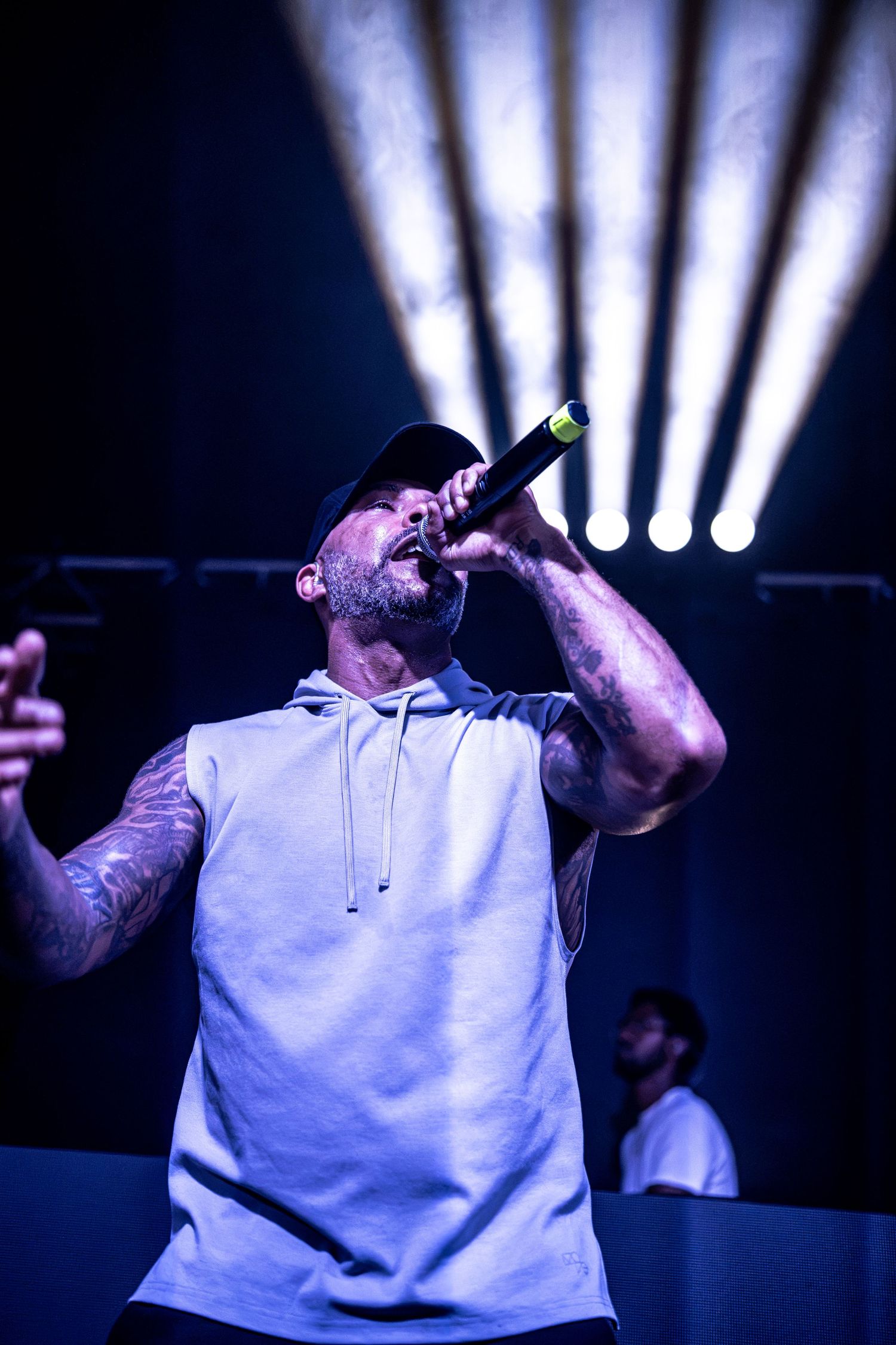 Tattooed male rapper singing into microphone on stage with dramatic blue stage lighting.