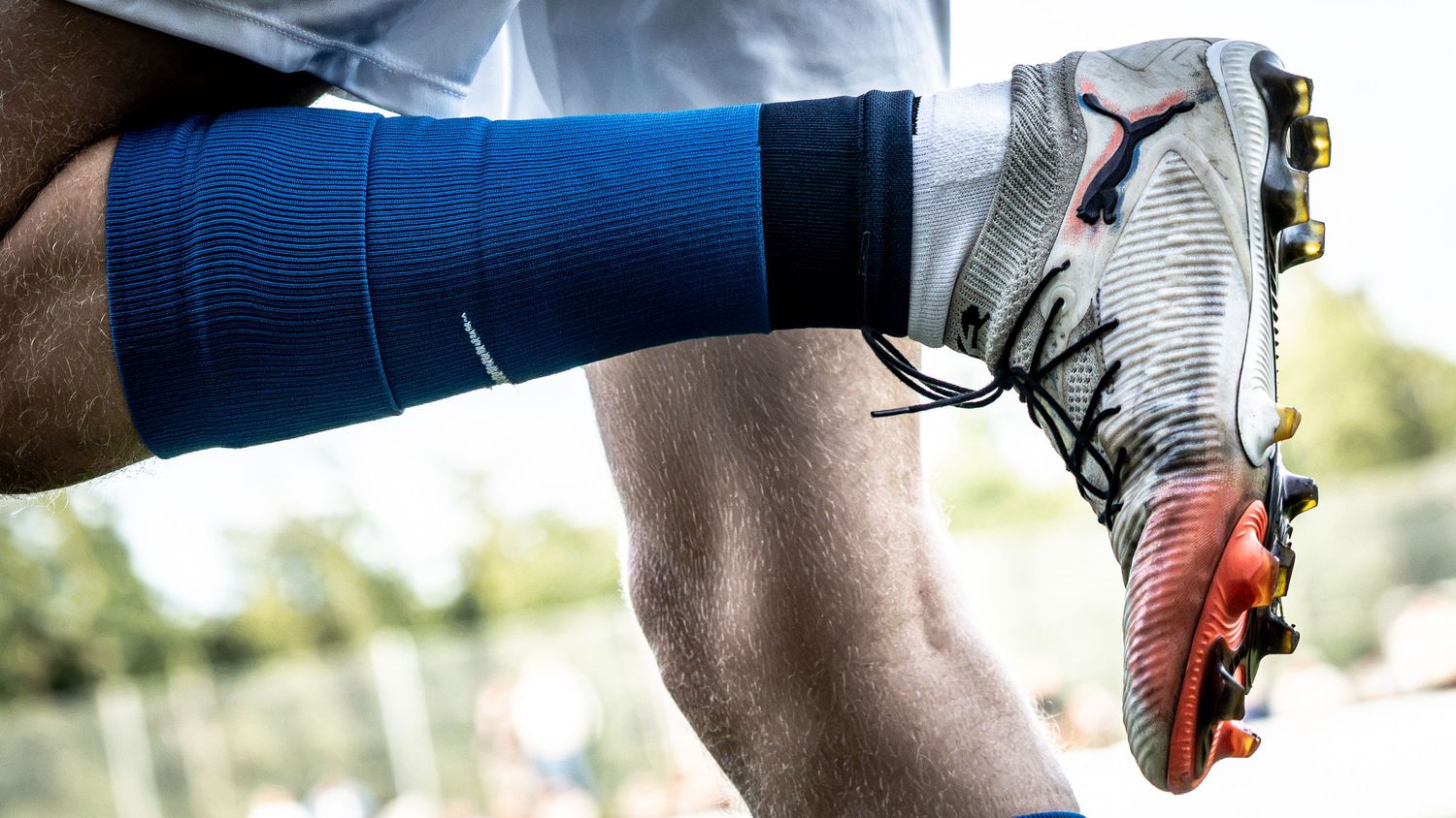 Close-up of a soccer player's legs wearing blue compression socks and Puma cleats on a grass field.