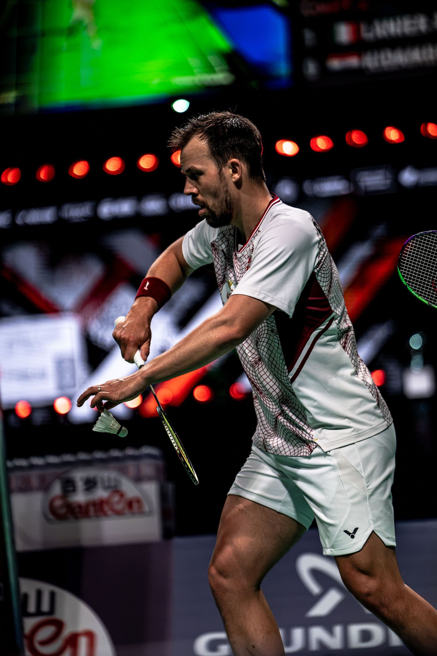 Male badminton player in white Victor kit executing a powerful backhand shot during BWF Thomas Cup Finals match.