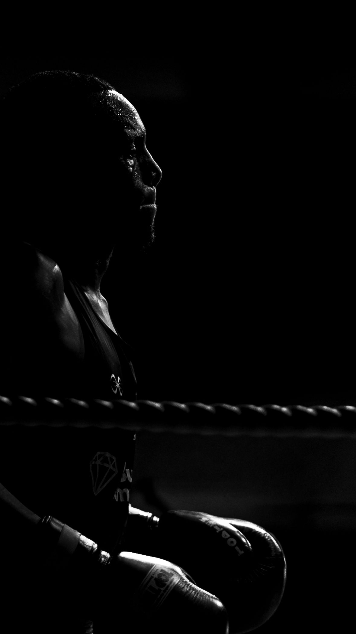 Dramatic black and white portrait of boxer resting in corner of ring with gloves.