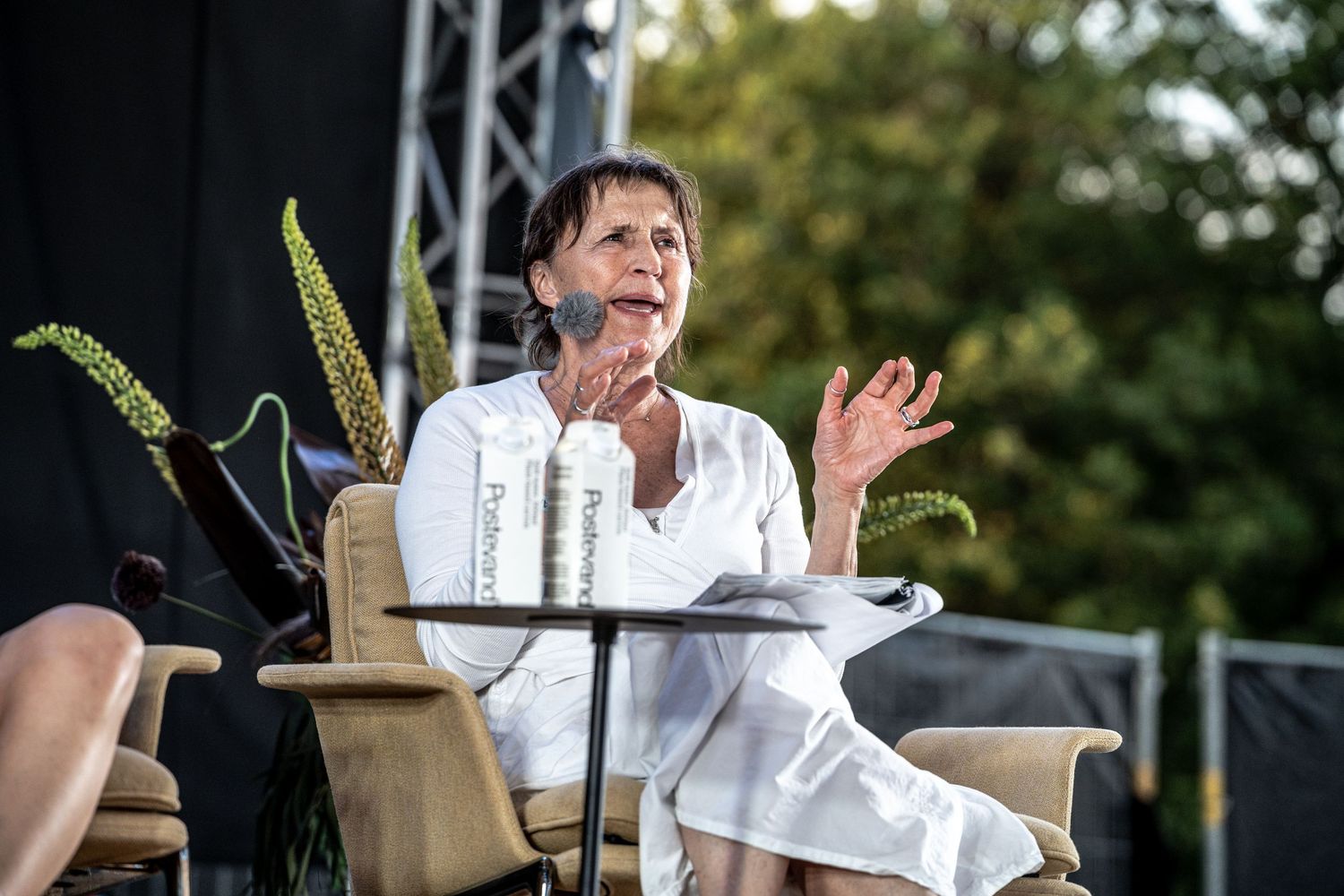 Close-up of a woman in white speaking passionately at an outdoor panel discussion.
