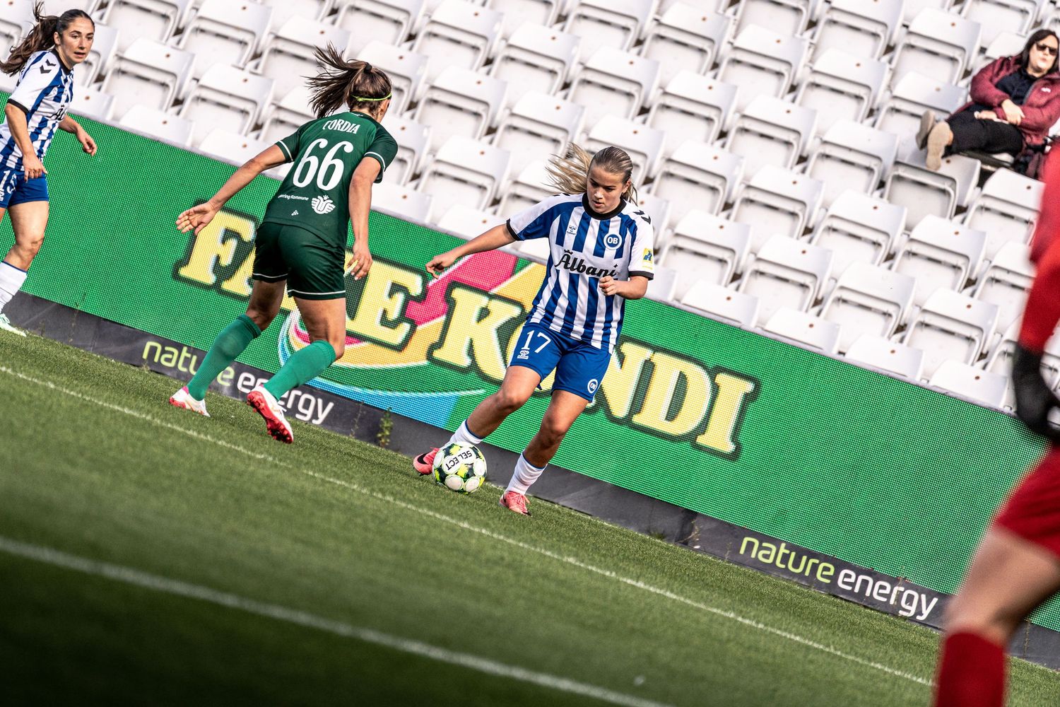 Women's soccer player in blue-white kit dribbles past opponent wearing number 66 green jersey.