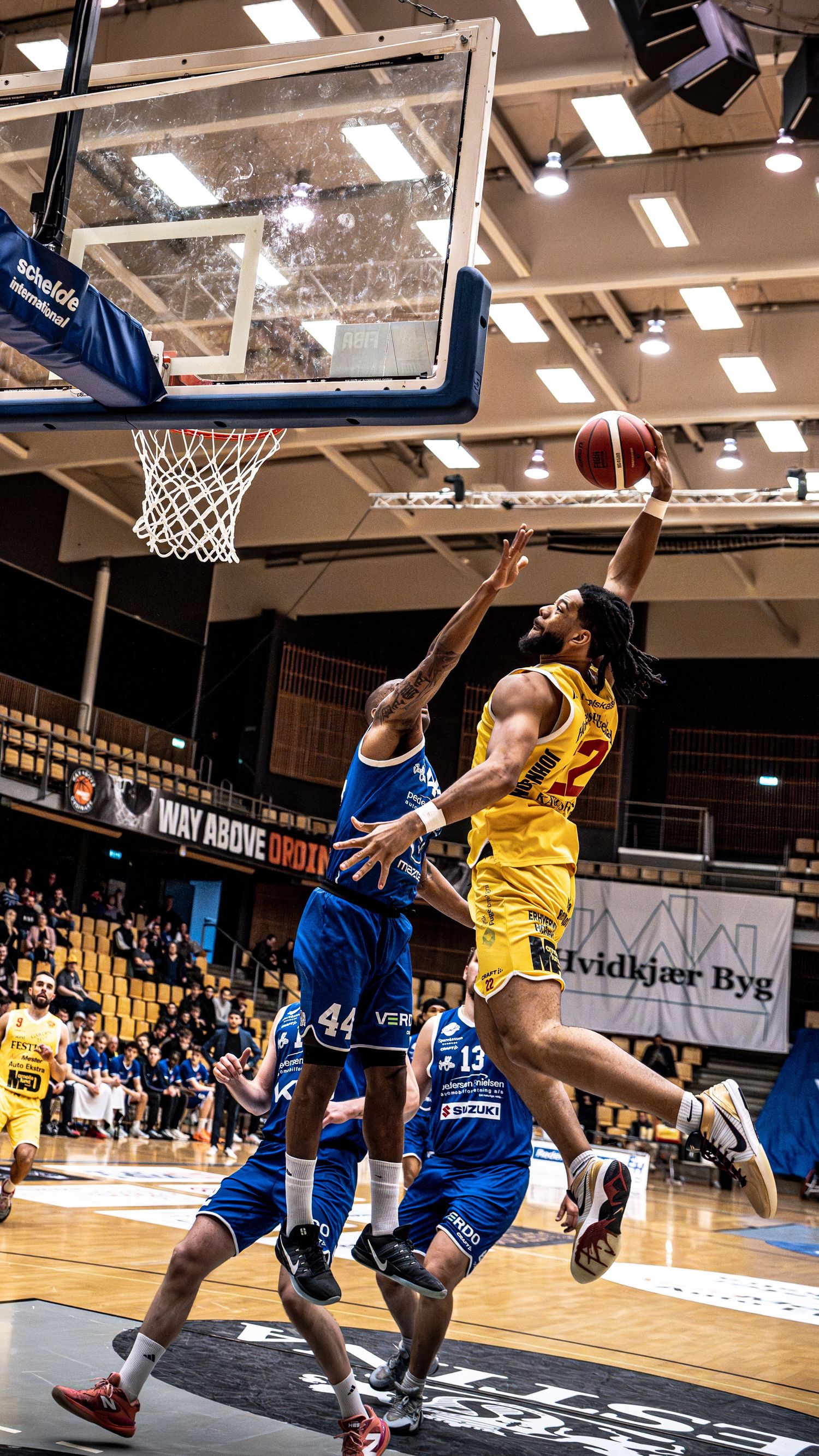 Basketball player number 22 in yellow performs a layup over blue team defenders.
