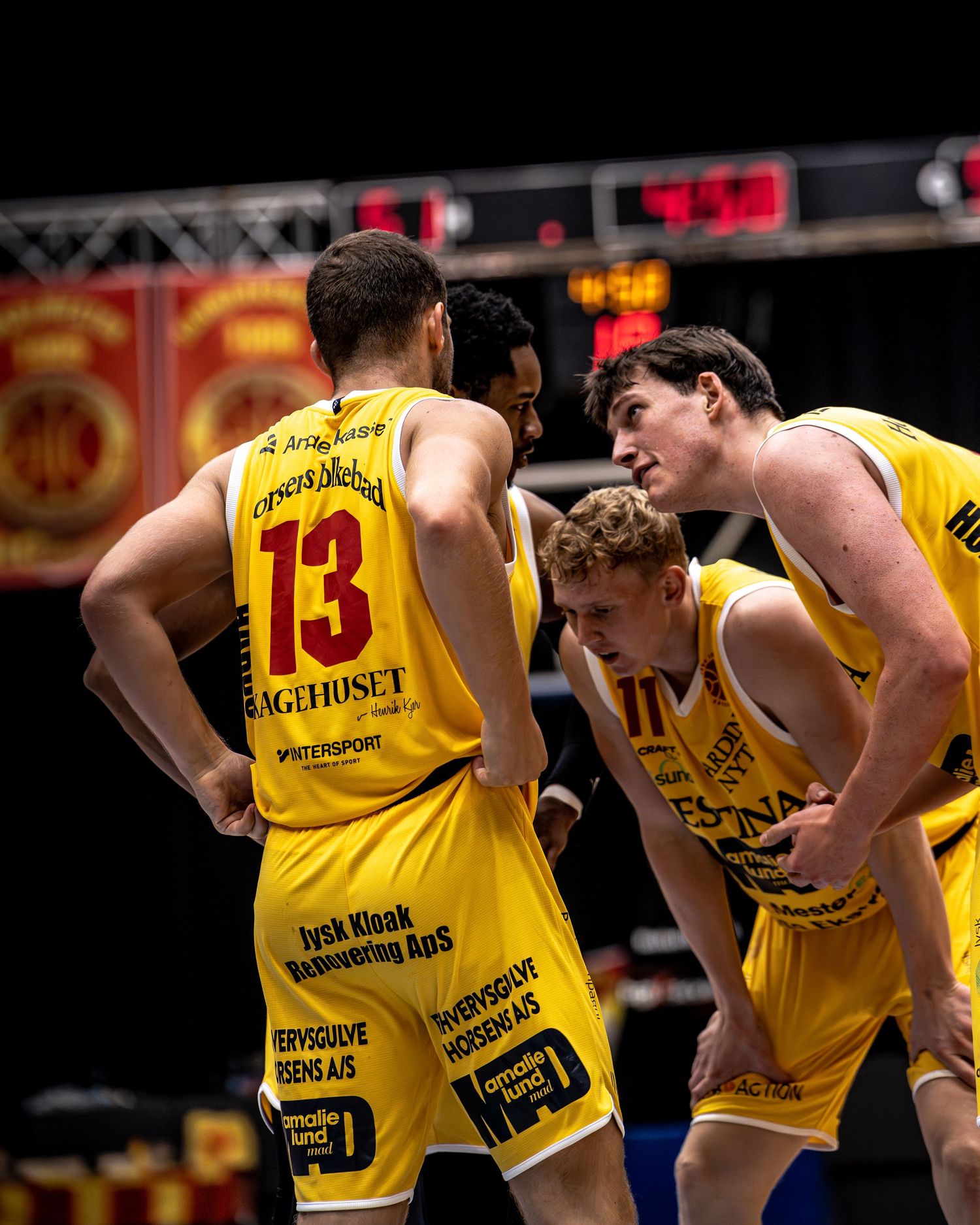 Three yellow-jersied basketball players huddling together during timeout on court.