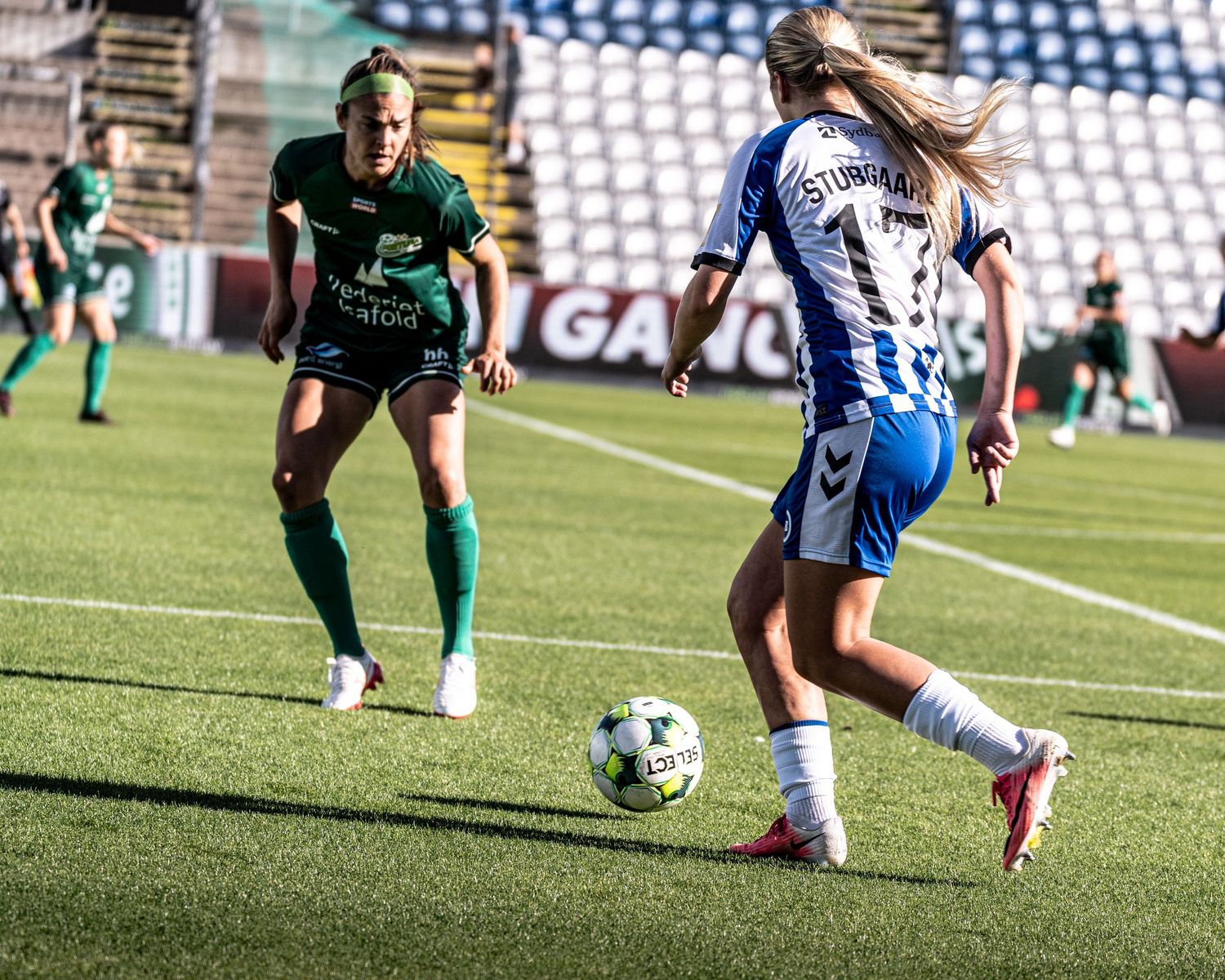 Female soccer players in green and blue-white kits battle for possession during women's football match.