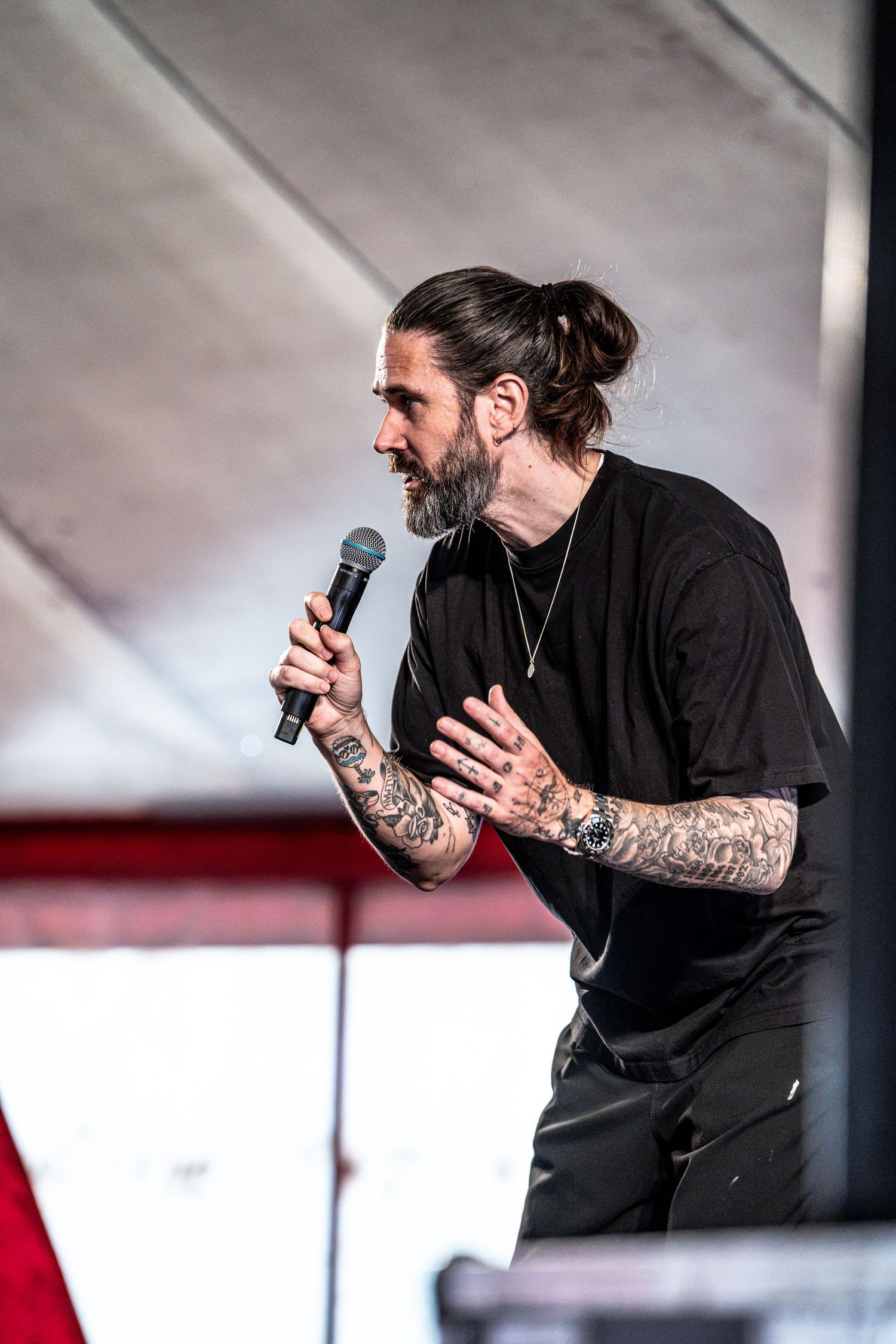 Side profile of tattooed man in black t-shirt holding microphone on stage.