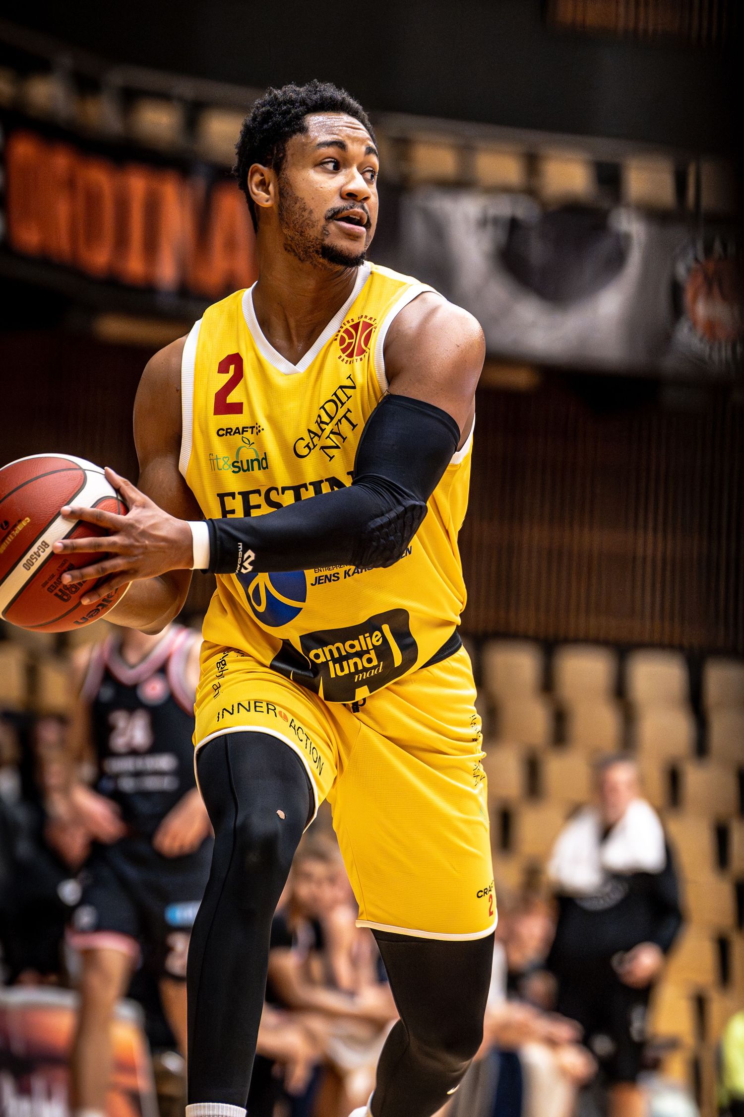 Yellow jersey basketball player number 2 prepares to pass ball during professional league game.