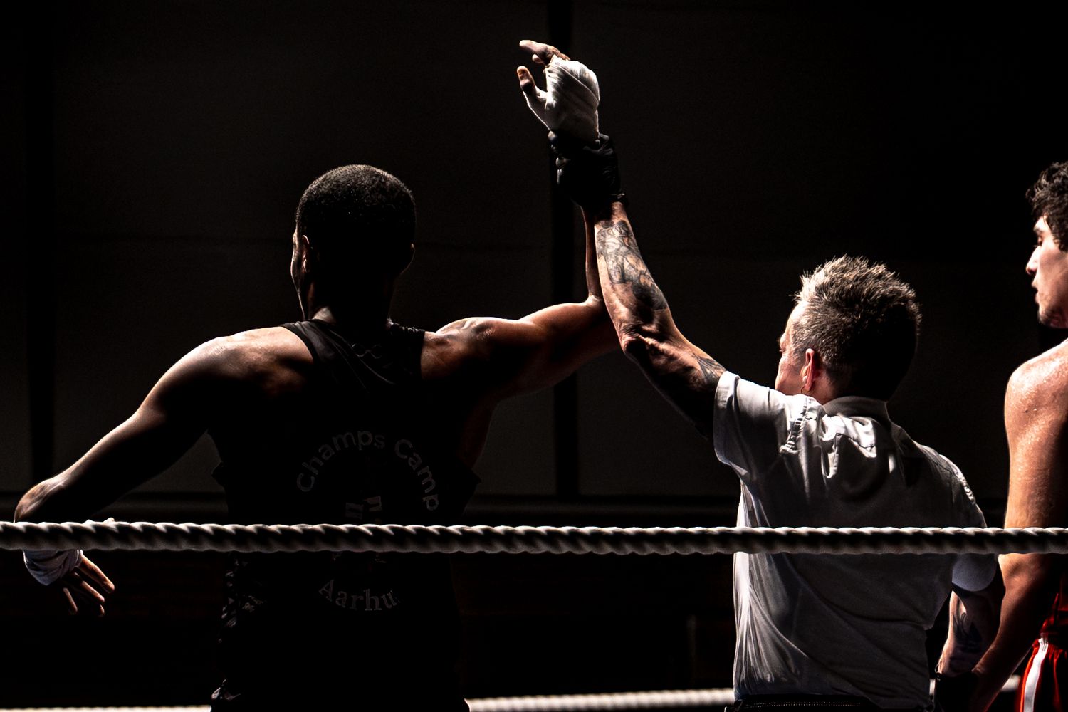 A referee raises a boxer's hand in victory after a boxing match in the ring.