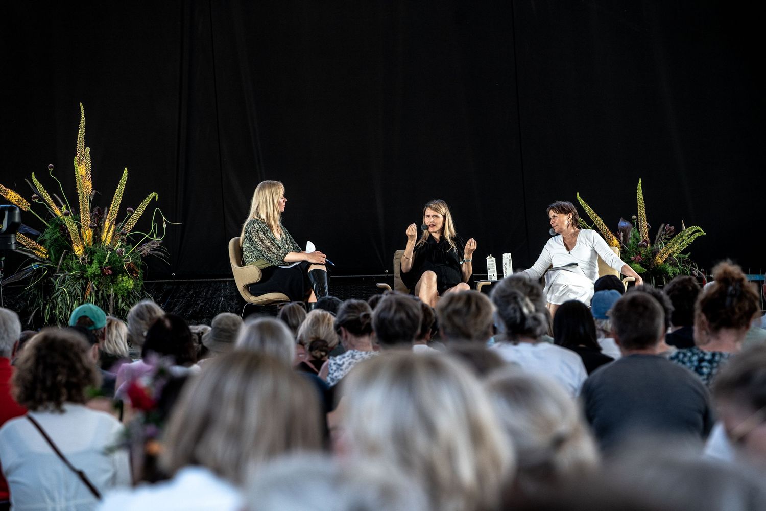 Three women on stage in lively panel discussion at outdoor festival.