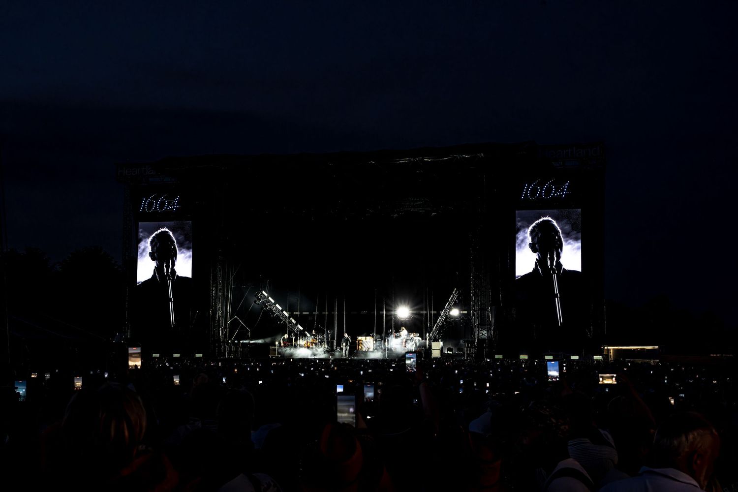 Dark concert stage with performer silhouetted on large screens at night festival.