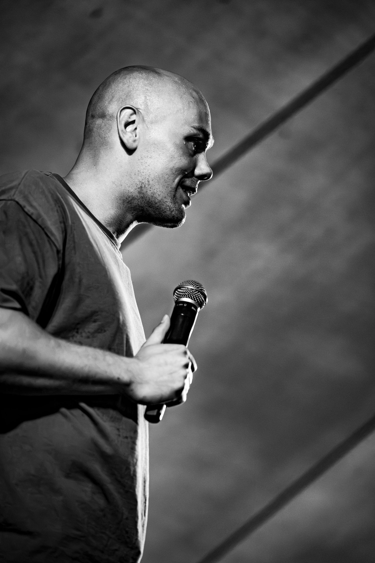 Black and white profile shot of bald man speaking passionately into microphone on stage.