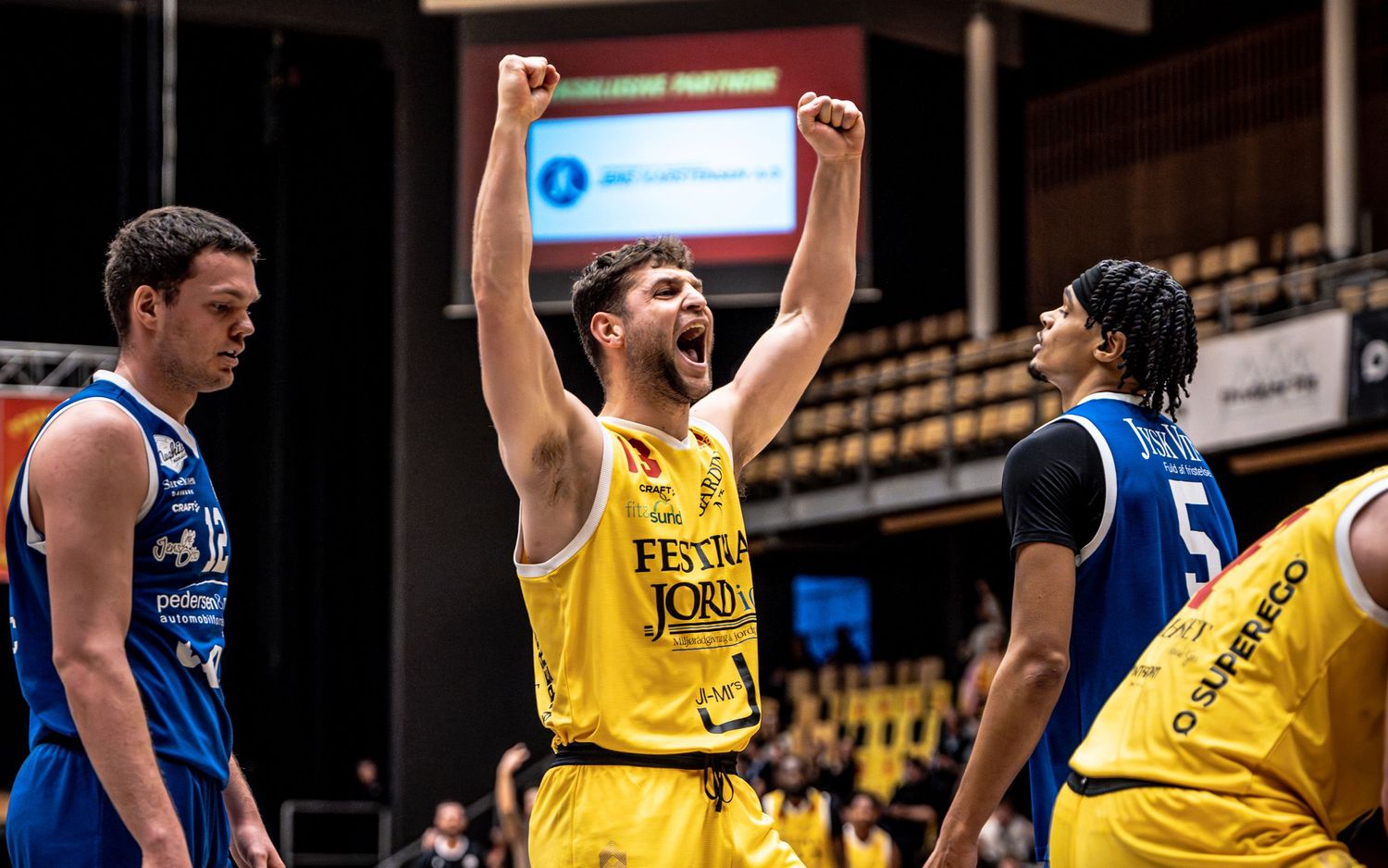 Yellow-jerseyied basketball player celebrates victory with raised fists during a professional basketball game.