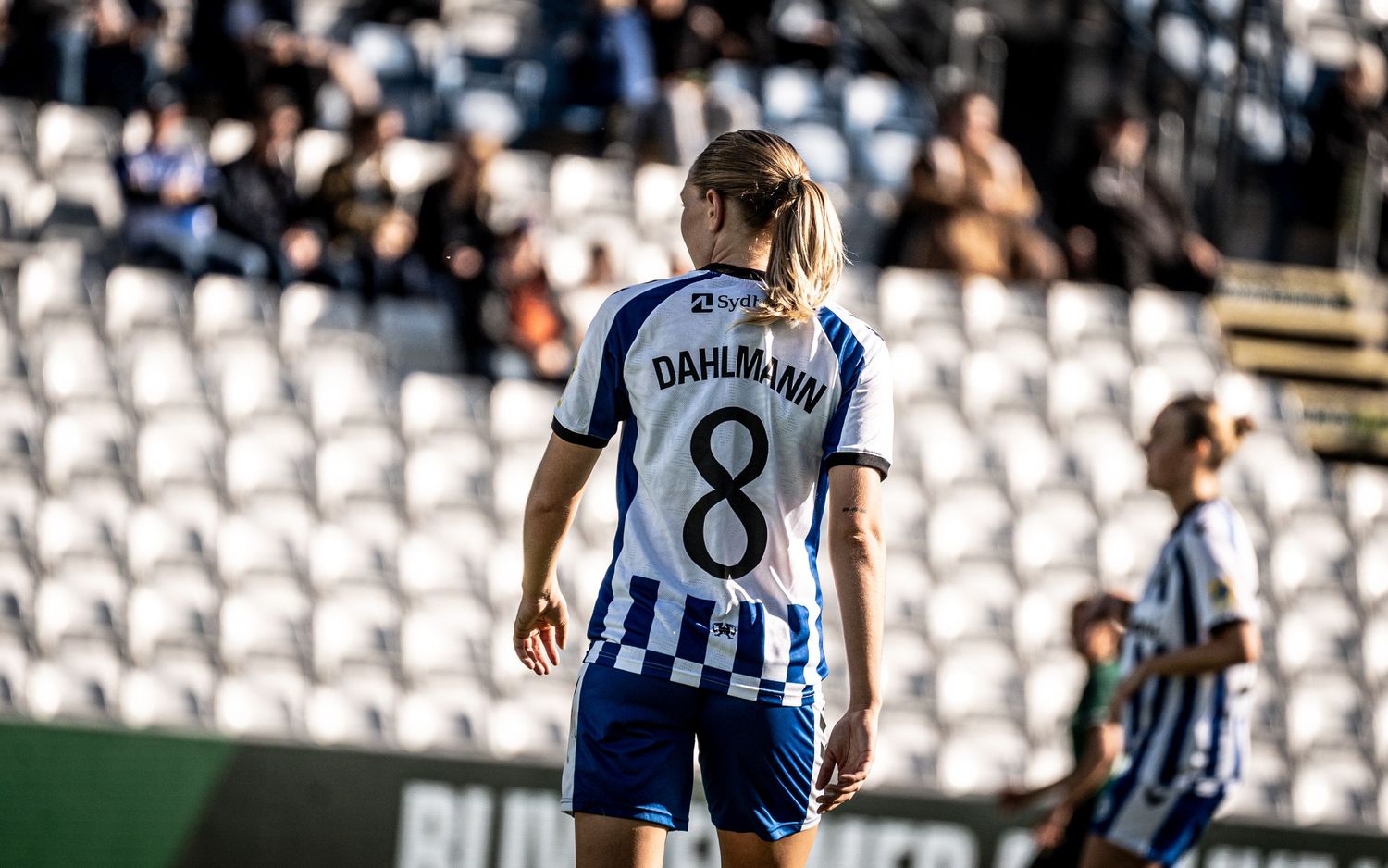 Female soccer player DAHLMANN number 8 in blue and white kit viewed from behind on stadium pitch.