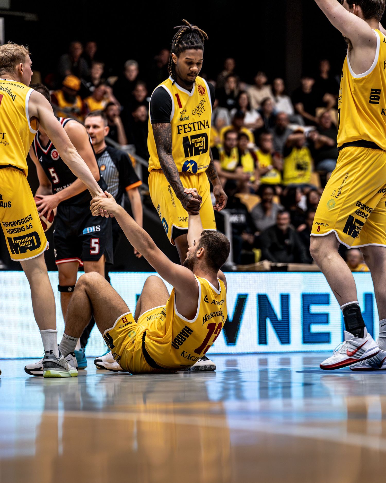 Yellow-jersied basketball player helping fallen teammate off court during game.