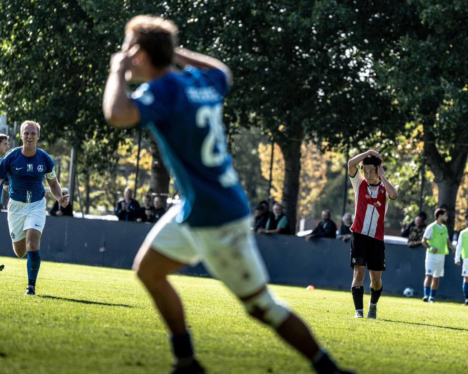 Blue-kitted soccer players celebrate a goal during an outdoor football match in autumn.