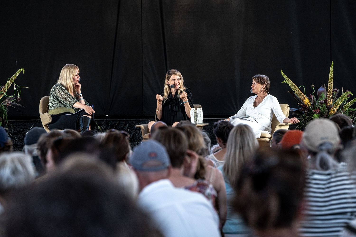 Three women engaged in panel discussion on outdoor festival stage.
