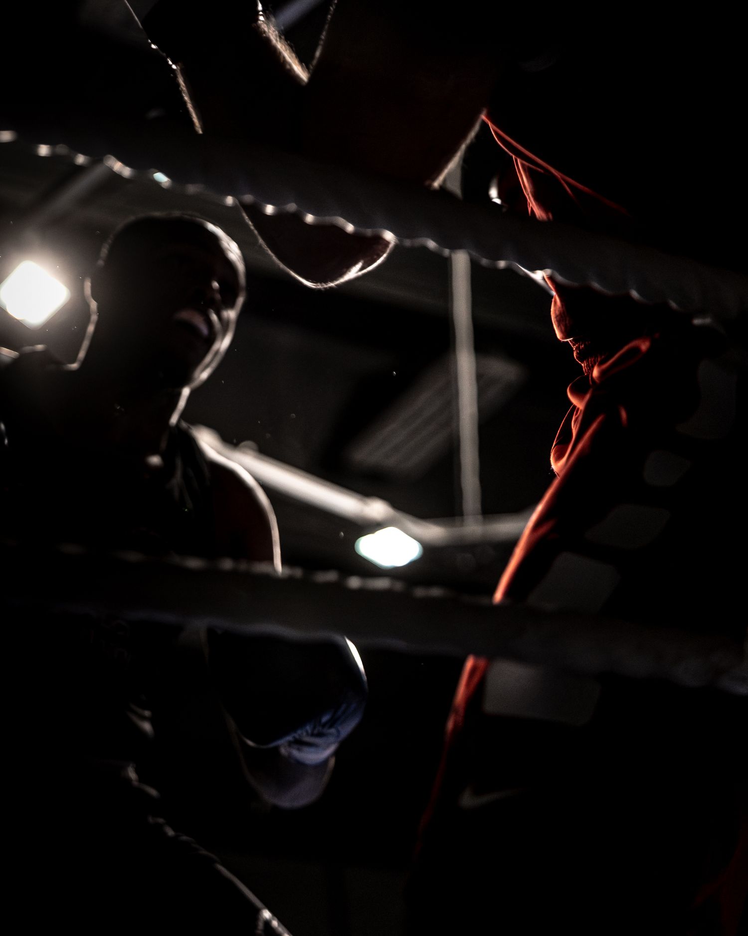 Two boxers face off in a dark boxing ring, illuminated by dramatic arena lighting.