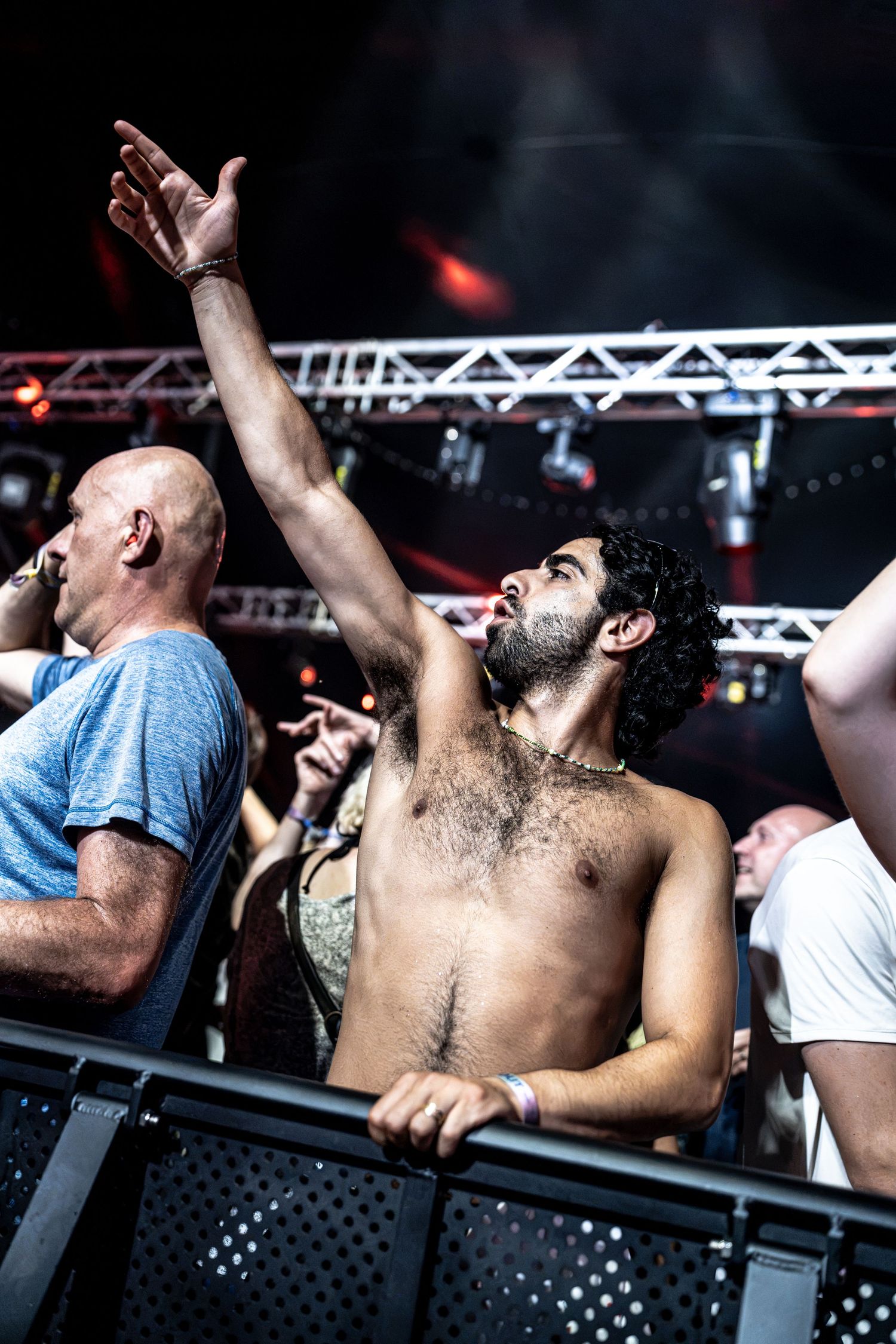Shirtless male fan raises hand in crowd at energetic live music concert event.