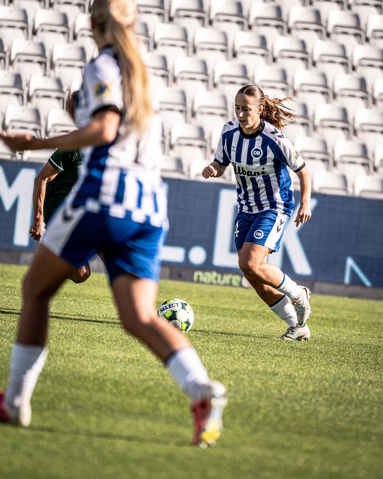 Two female soccer players in blue and white uniforms compete for ball on green stadium pitch.