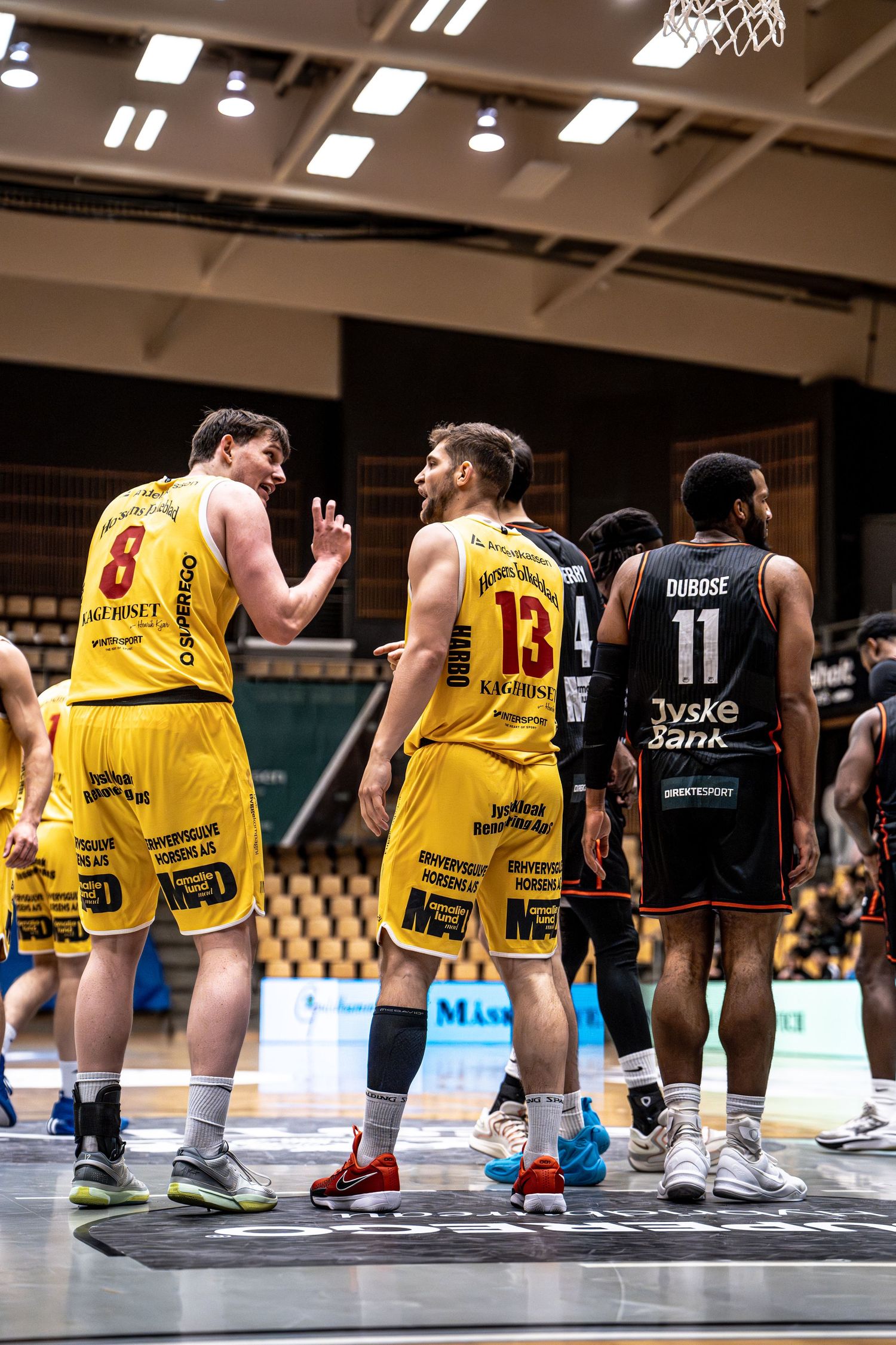 Two yellow-uniformed basketball players numbered 8 and 13 talk during a game break.