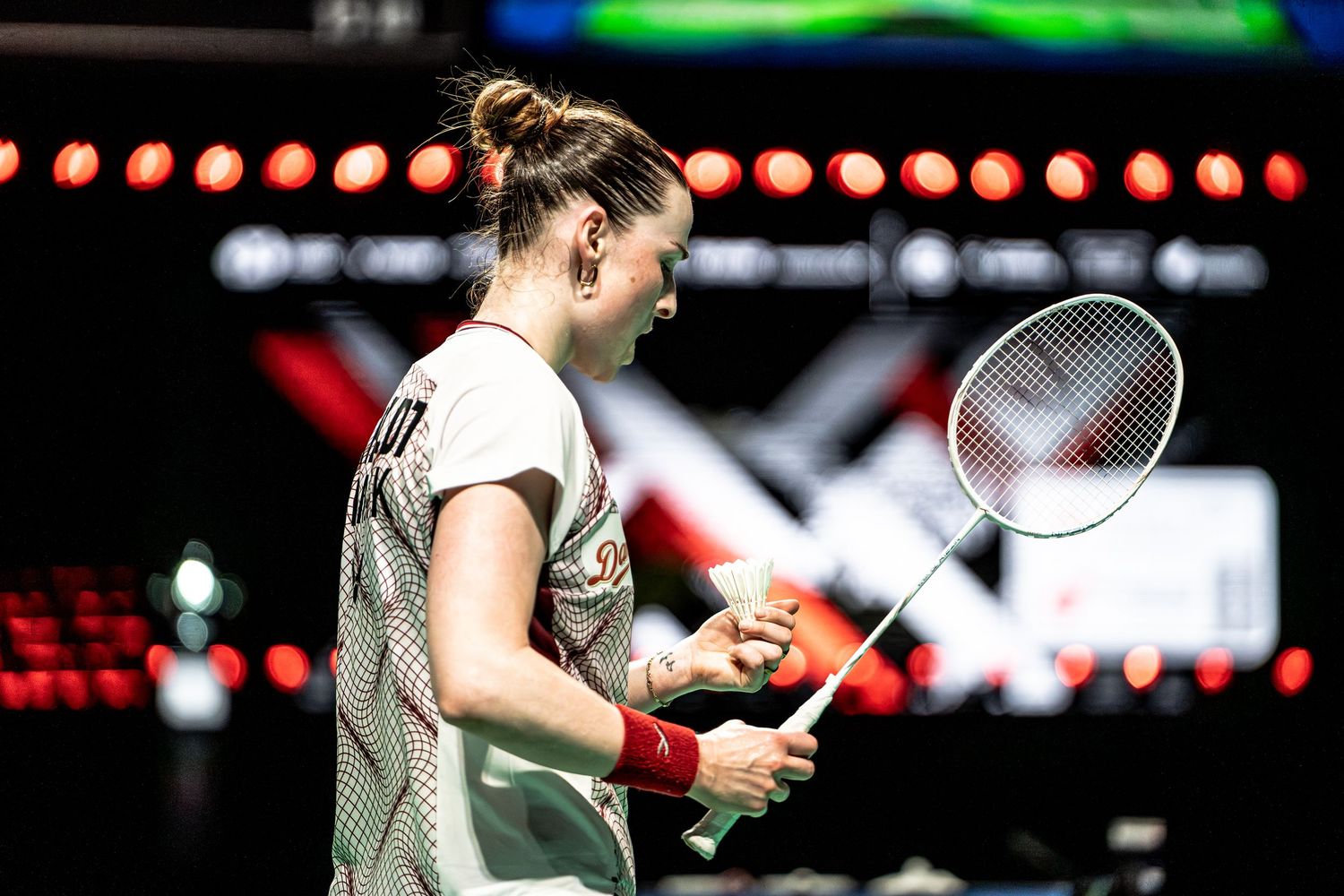 Female badminton player holding shuttlecock and racket preparing to serve during an indoor badminton tournament.