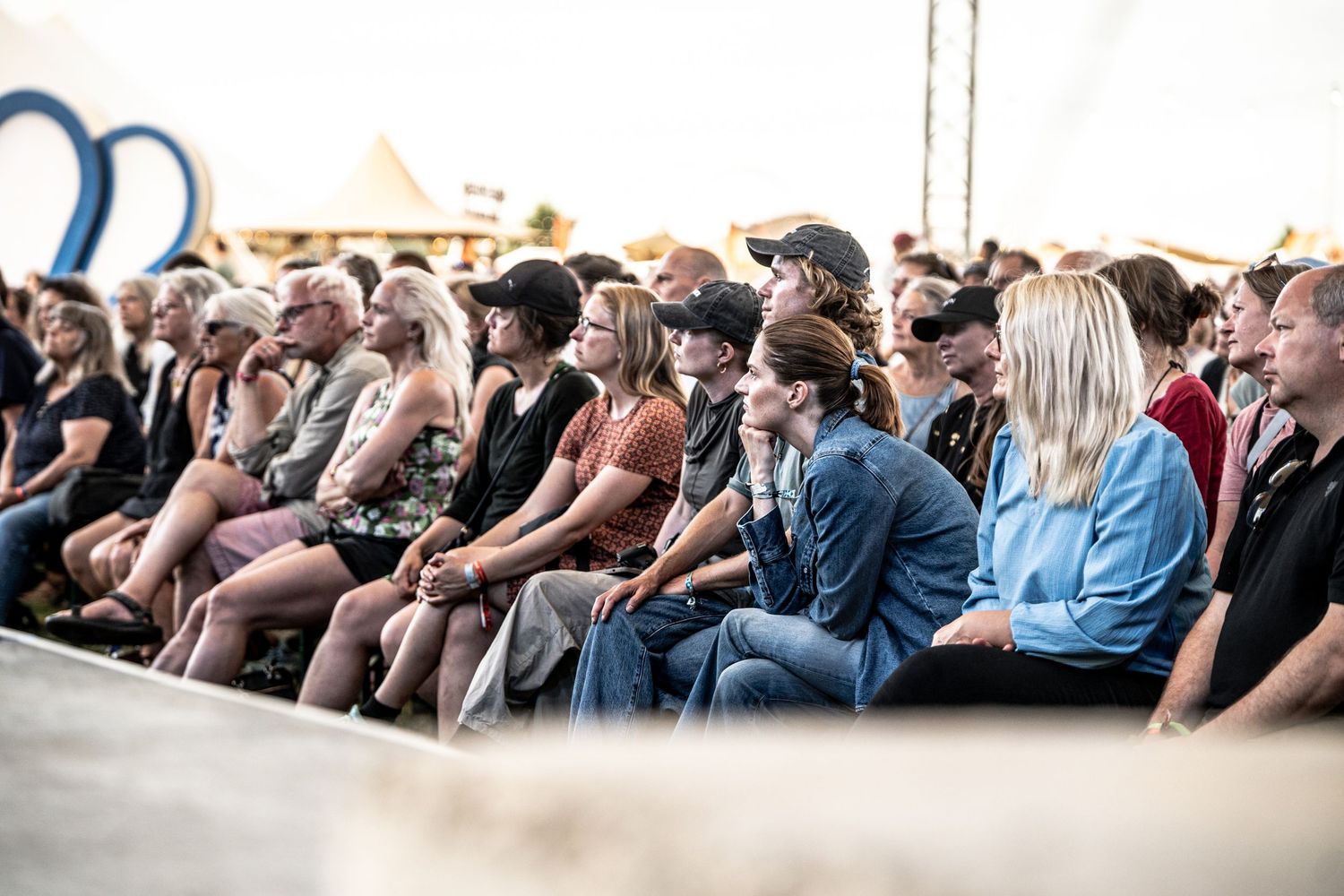Crowd of diverse attendees seated and watching a performance at an outdoor summer festival.