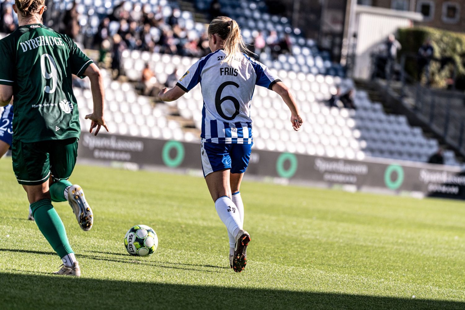 Female soccer player number 6 in blue and white kit controls ball during competitive stadium match.