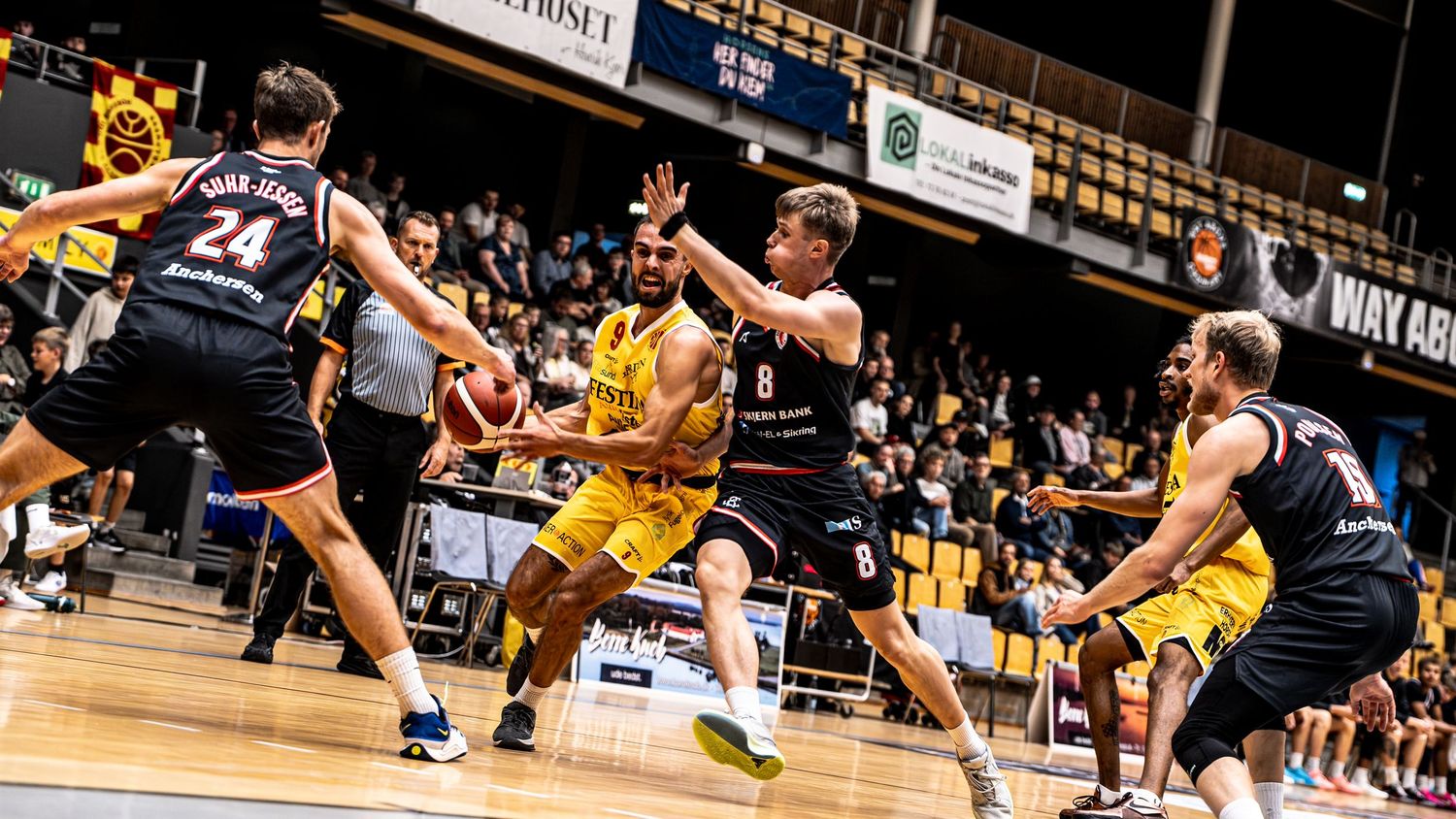 Yellow team player drives through defenders in an intense professional basketball game action shot.