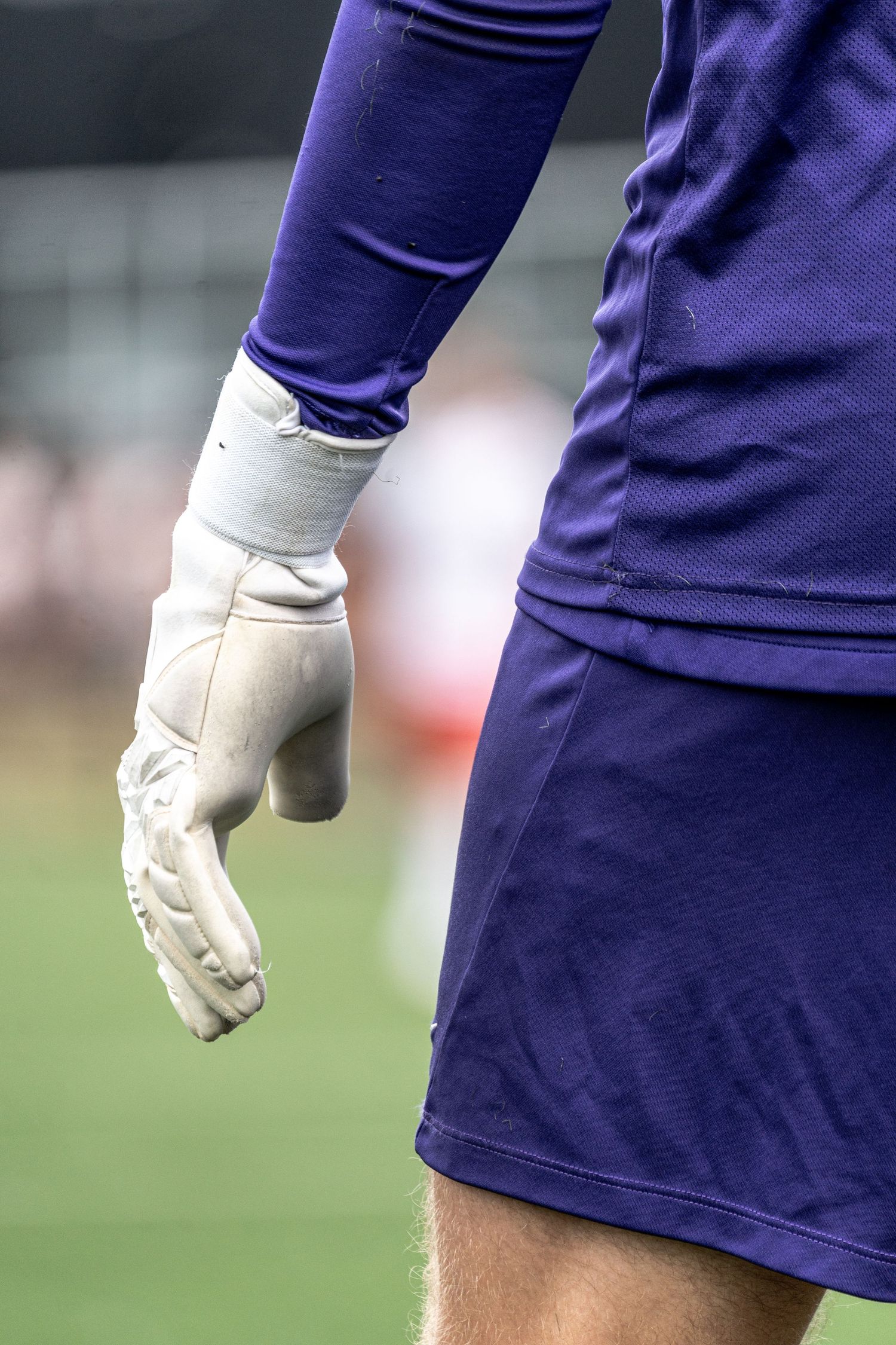 Close-up of a soccer goalkeeper wearing purple uniform and white gloves during a match.