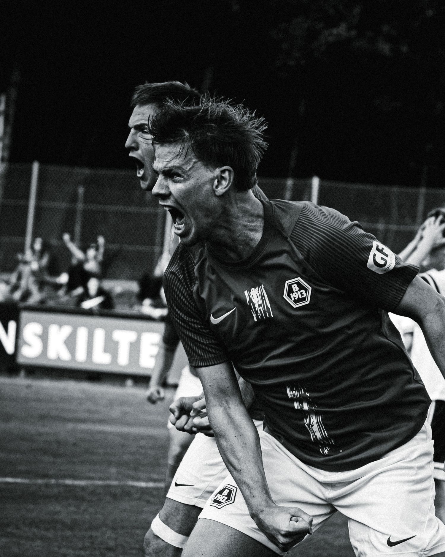 Two soccer players celebrate a goal intensely on the field in a black and white photo during a match.