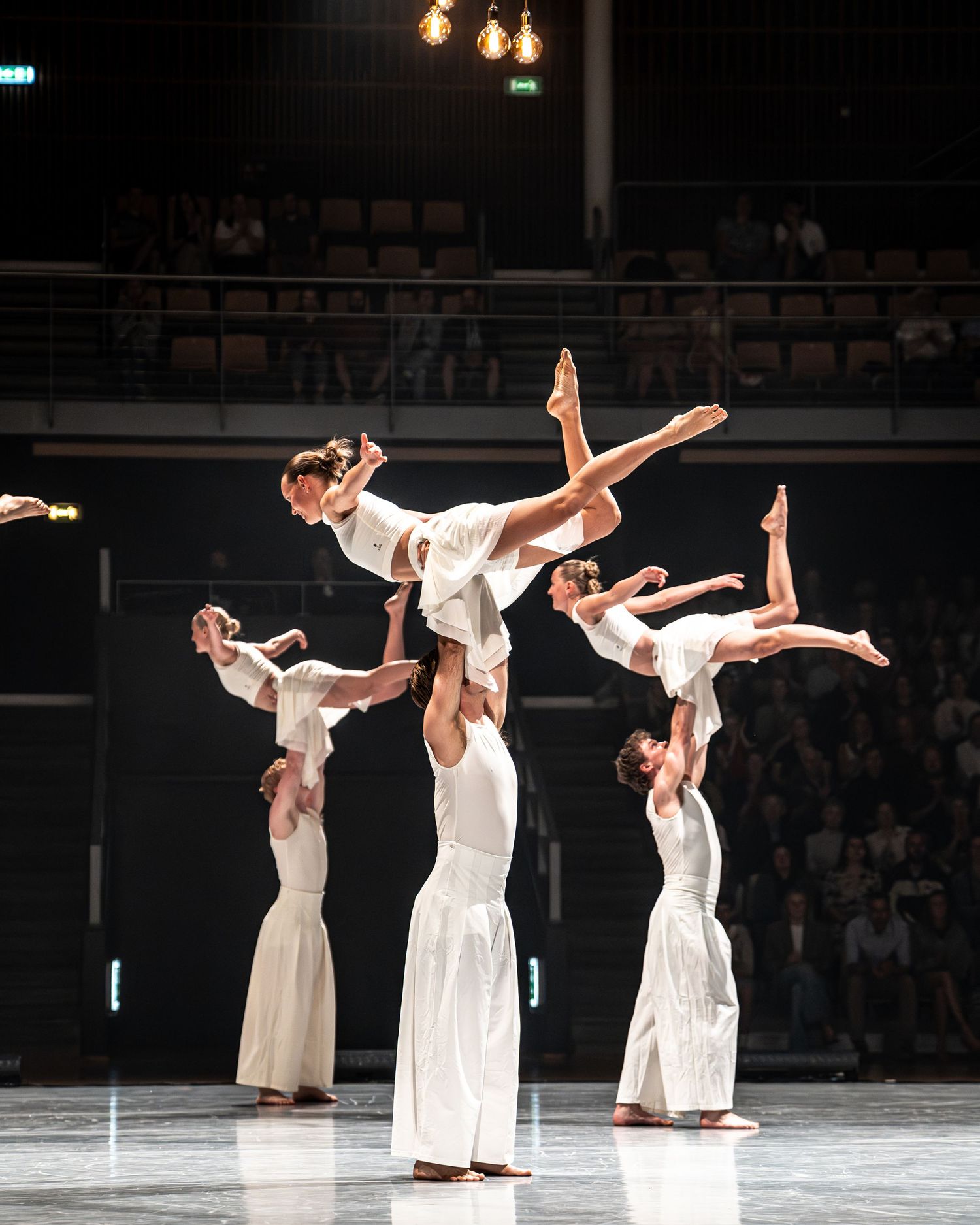 Acrobatic dancers in white costumes perform stunning lifts on stage during a live dance performance.