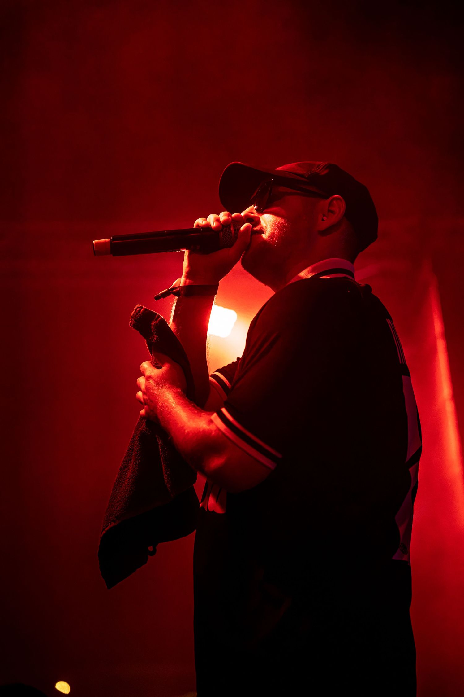 Hip-hop artist performing on stage bathed in dramatic red lighting holding microphone close.