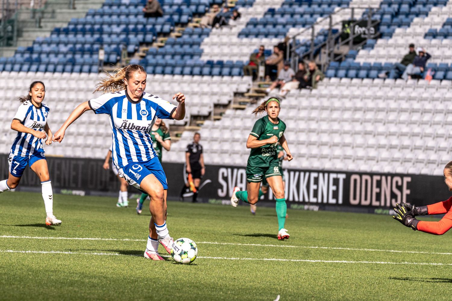 Women's soccer player in OB blue-white kit breaks away with ball during competitive match in Odense.