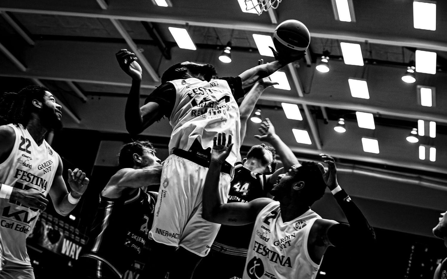 Black and white photo of basketball players jumping for the ball during intense game action.
