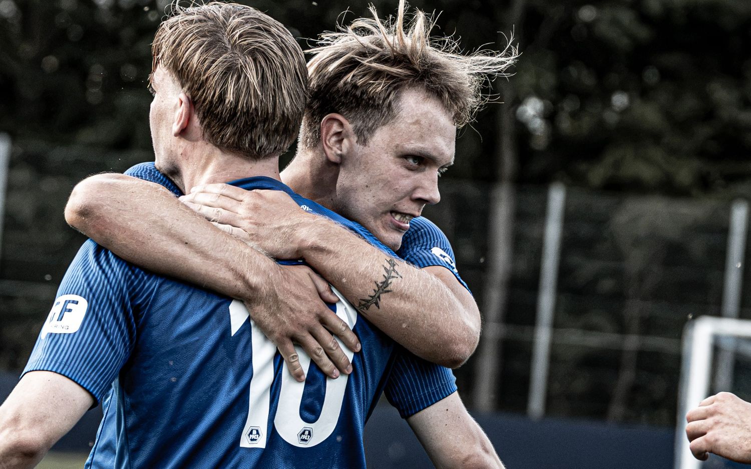 Two soccer players in blue jerseys celebrate together on the field, embracing after a goal.