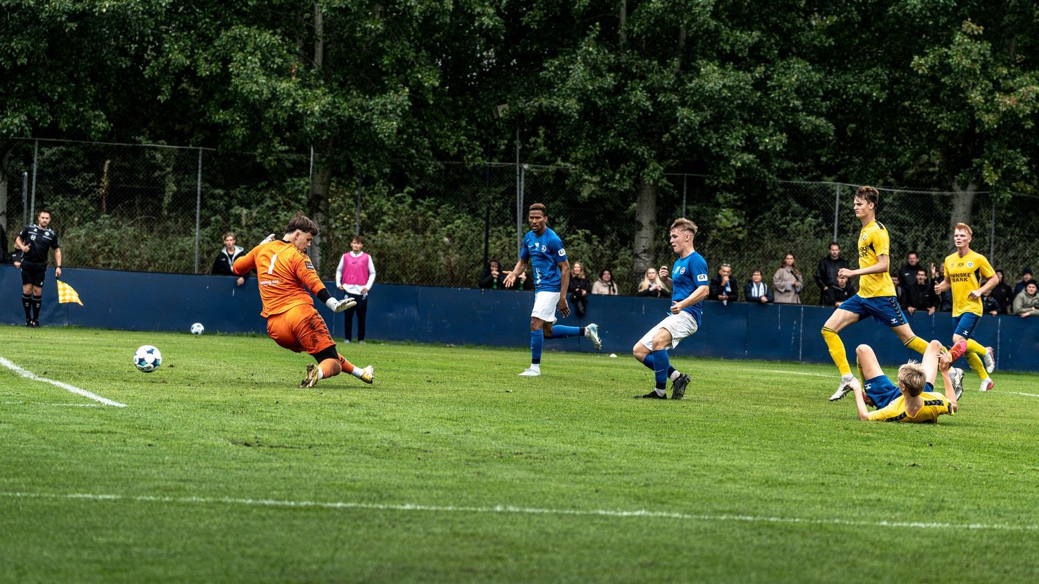 Soccer player shoots on goal while goalkeeper dives to make a save during a match.