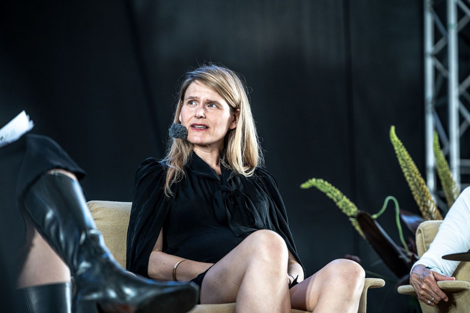 Woman in black velvet dress seated on stage looking upward at an outdoor panel event.