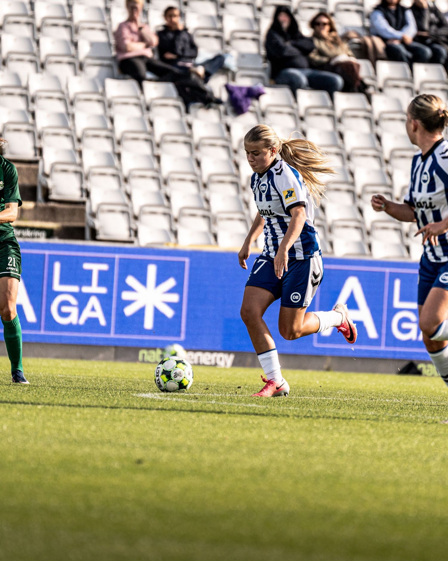 Female soccer player in blue and white kit dribbling past opponents during a Liga league match.