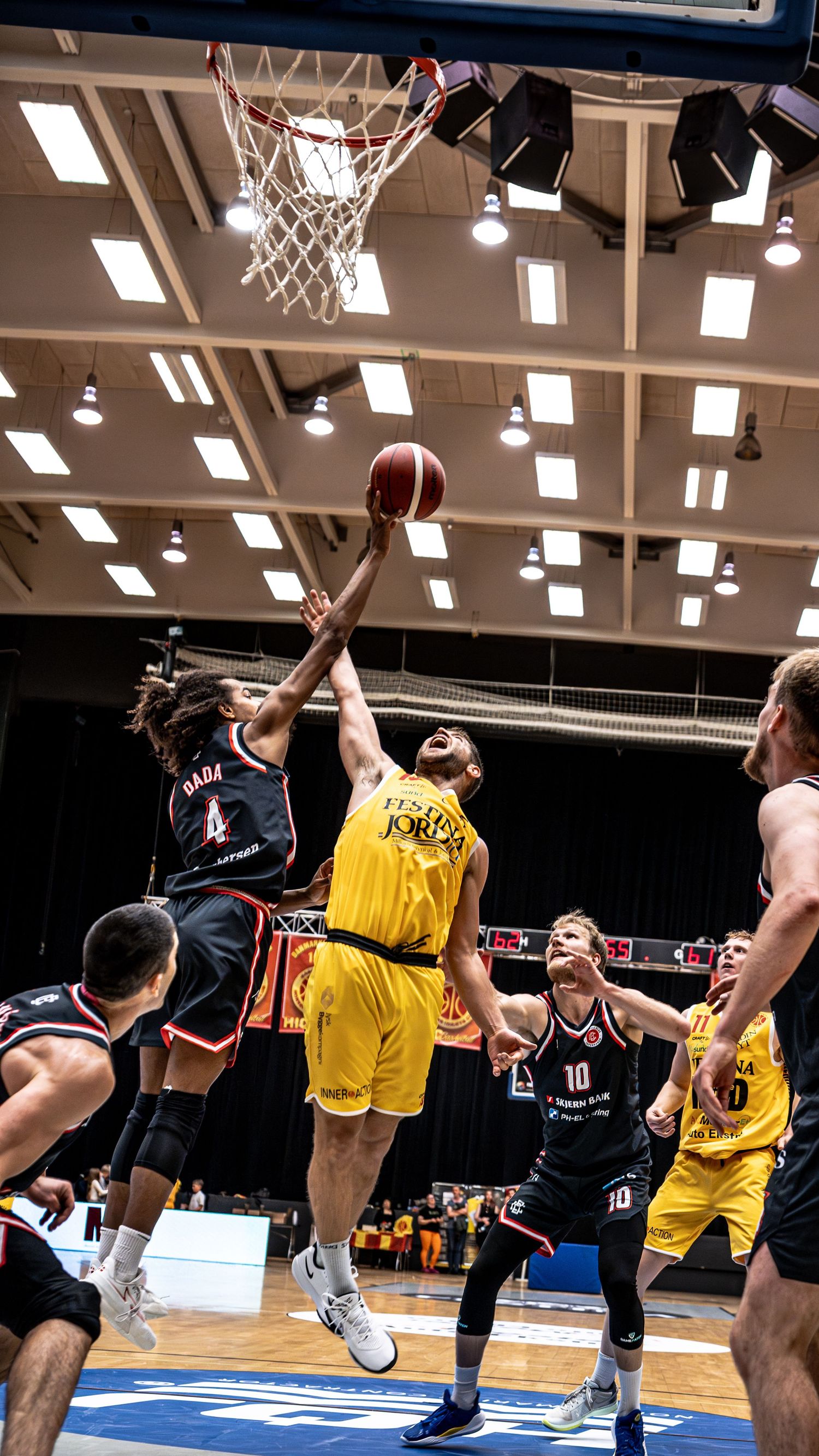 Players competing for rebound near basket during intense basketball game action.