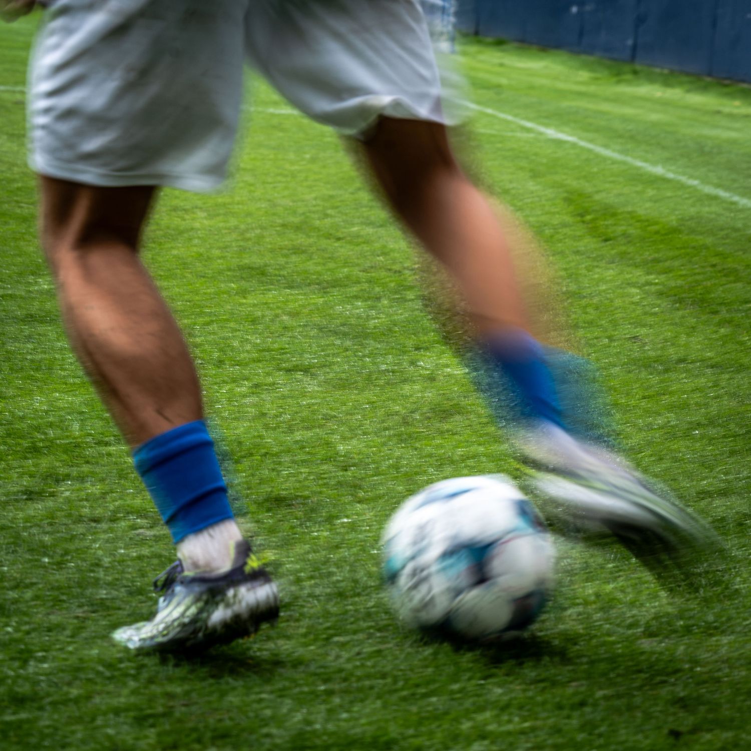 Blurred motion shot of soccer player in blue socks dribbling ball on green turf.