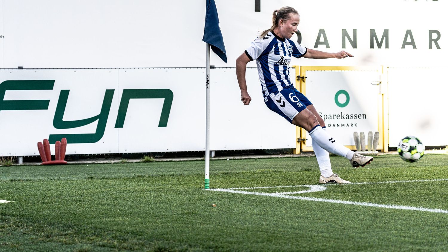 Female soccer player in blue and white kit takes corner kick during outdoor football match.