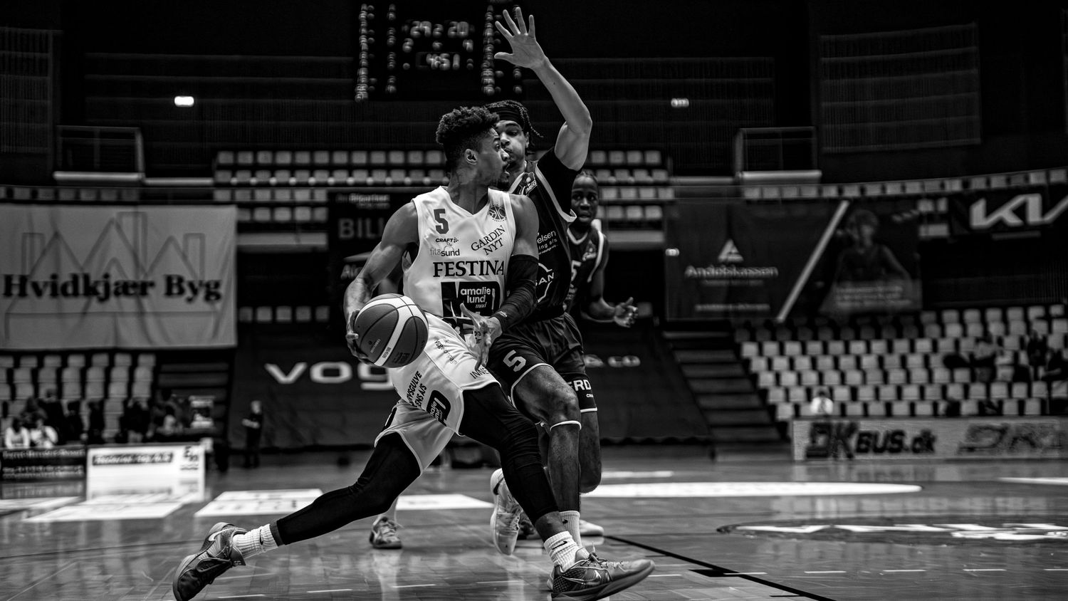 Black and white photo of basketball player driving past defender in professional league game.
