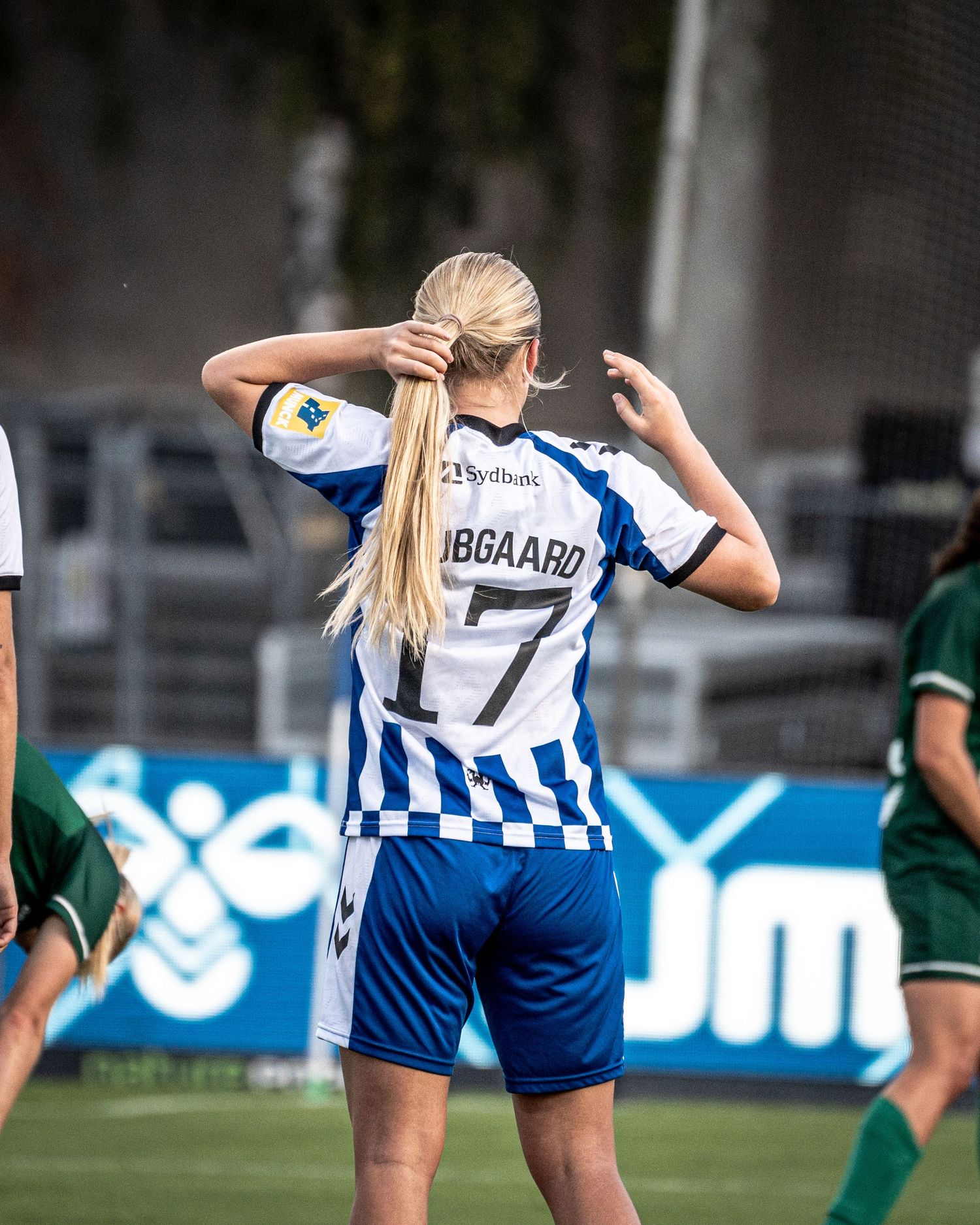 Women's soccer player in blue and white dribbles past a green-kitted opponent numbered 21 on the field.